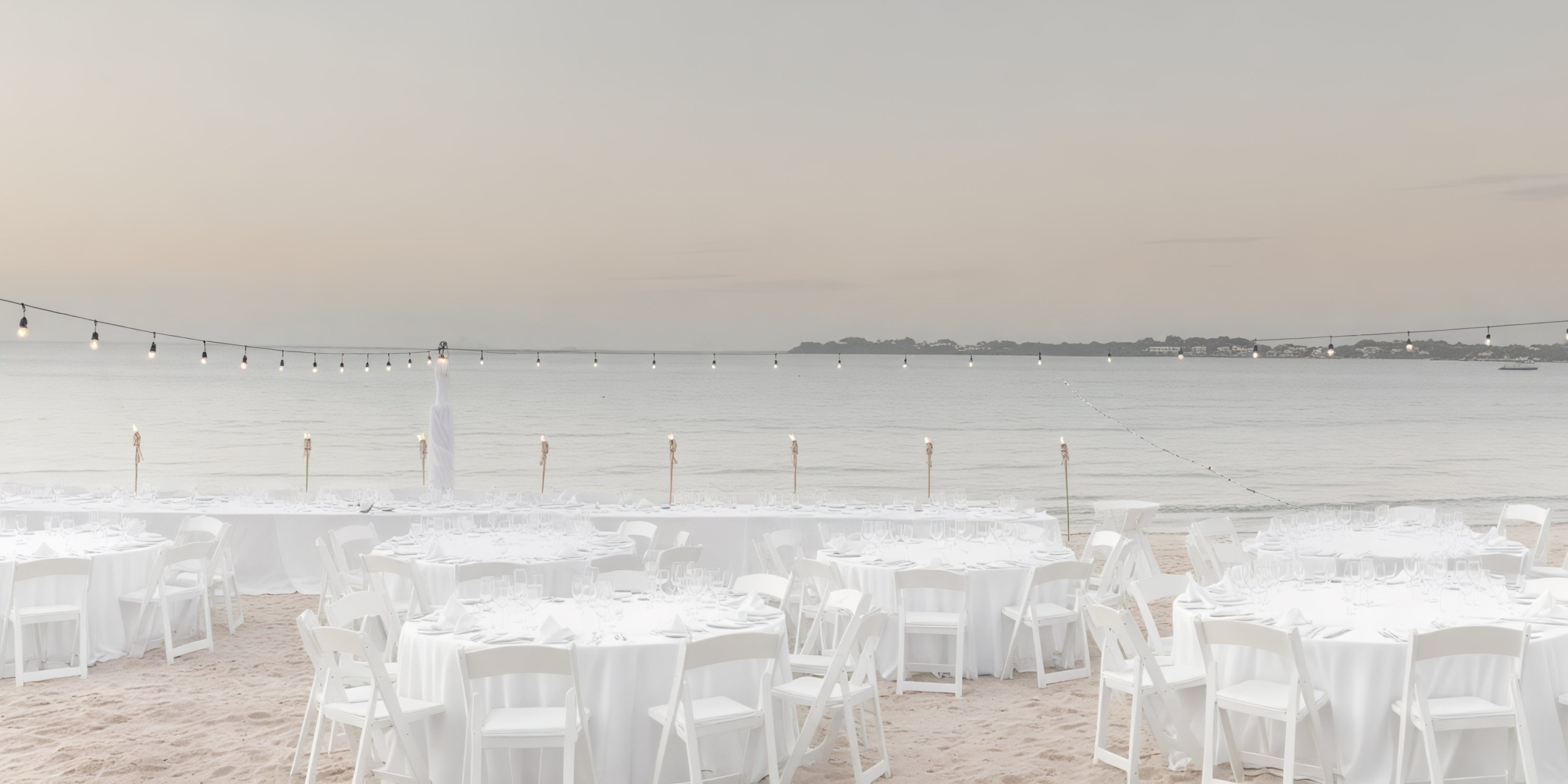 Set against the stunning backdrop of Hideaway at Royalton Negril, this destination wedding features a picturesque beachfront setup complete with elegant white tables, chairs, and twinkling lights.