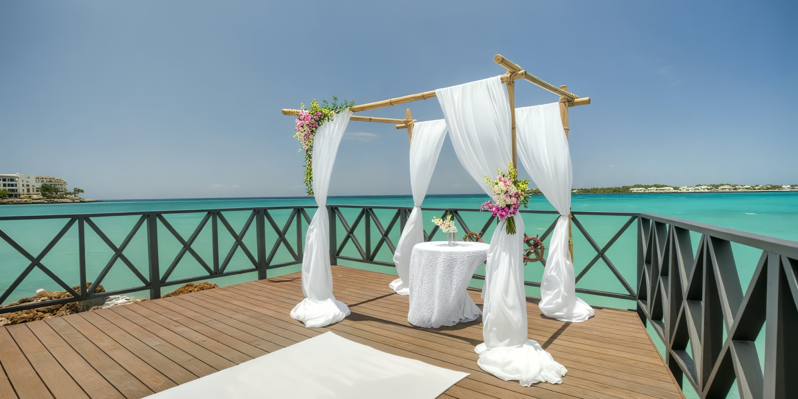 A deck featuring a wedding altar, elegantly draped in white fabric, offers a stunning view of the turquoise ocean—perfect for a destination wedding.