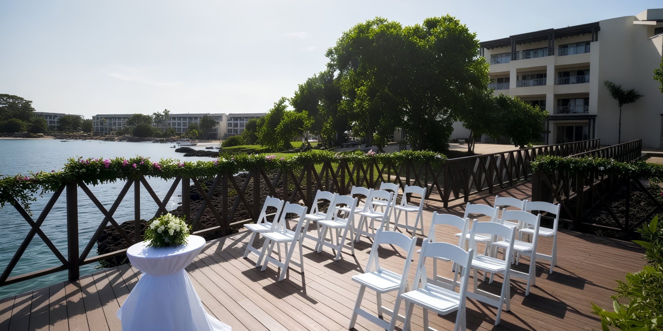 An enchanting destination wedding setup featuring a charming arrangement of white chairs on a wooden deck, situated beautifully by the water.