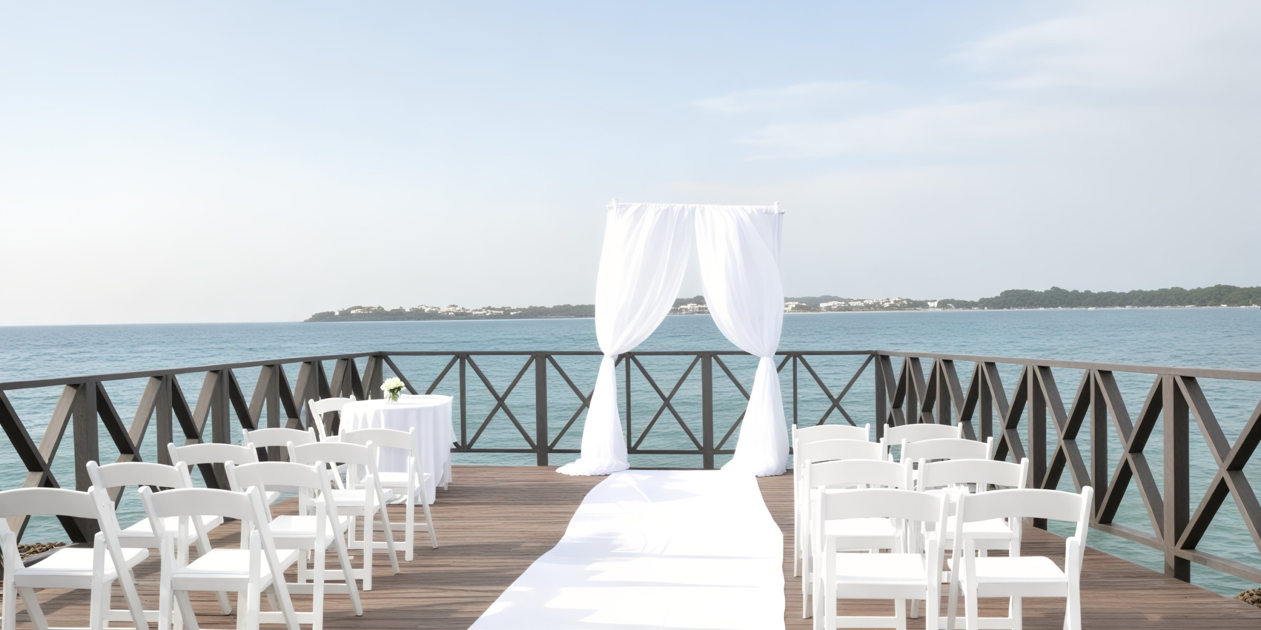 A picturesque destination wedding set up on a pier with stunning ocean views, featuring an elegant arrangement of white chairs and a beautifully adorned arch.