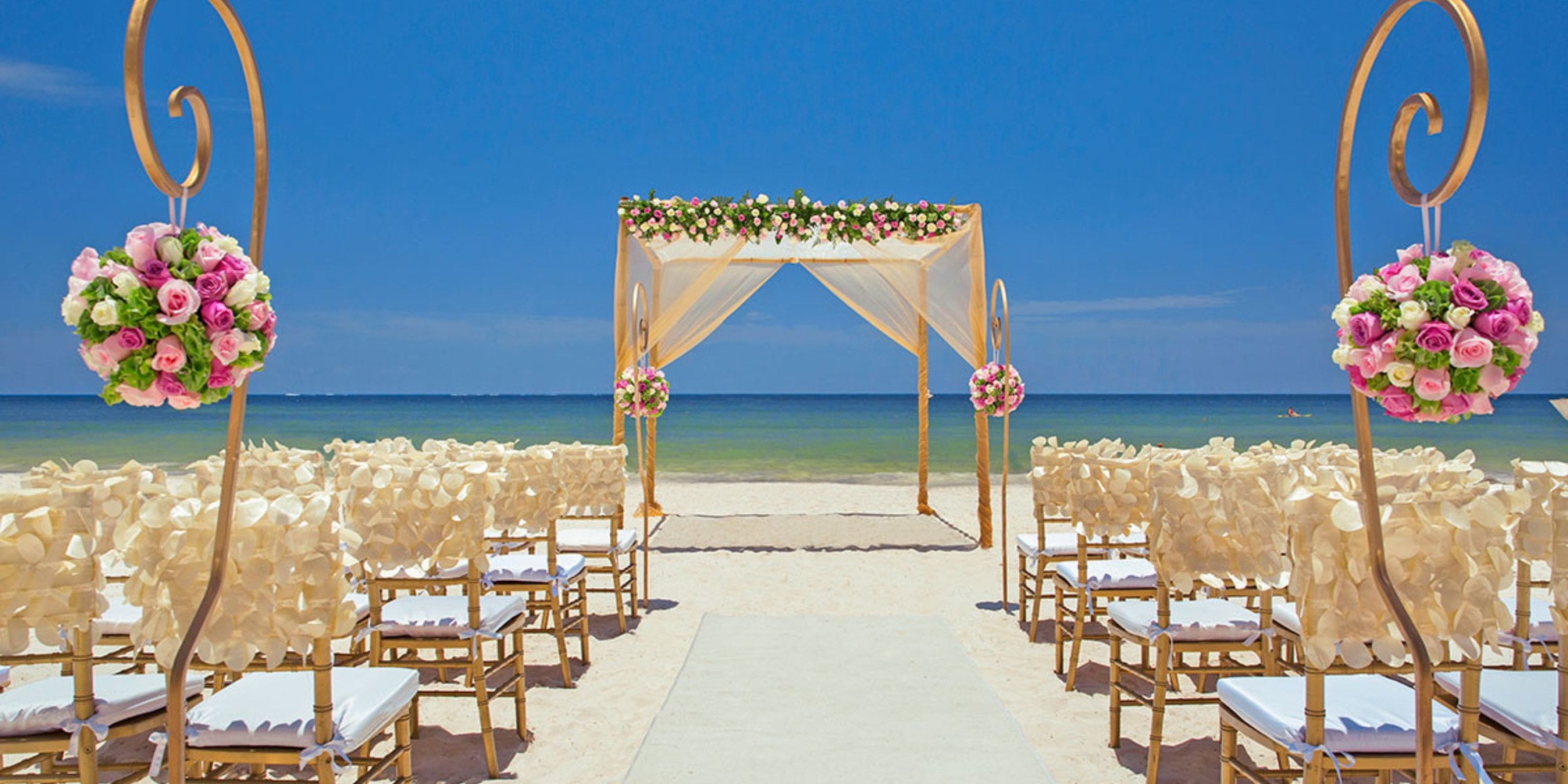 Wedding setup at Hideaway, Royalton Riviera Cancun featuring floral decor and chairs elegantly arranged to face a stunning sea arch.