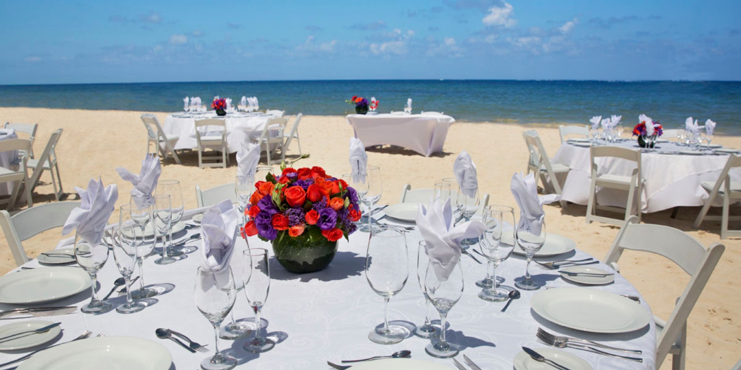 Tables are elegantly arranged at Hideaway @ Royalton Riviera Cancun on a sandy beach, providing stunning ocean views—perfect for a beautiful destination wedding.