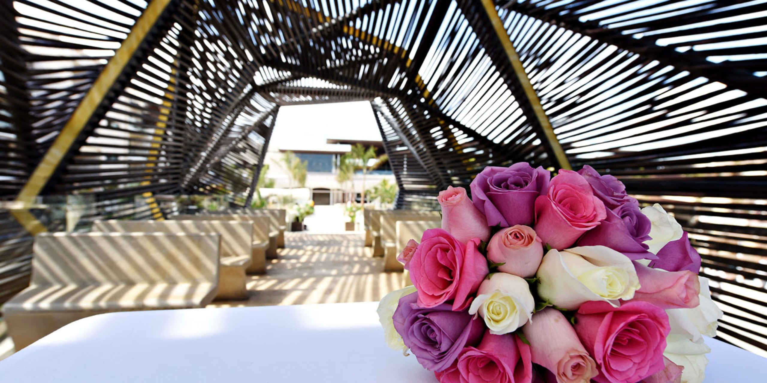 A bouquet of roses arranged in a geometric-design pavilion with wooden benches, perfect for a destination wedding at Royalton Riviera Cancun.