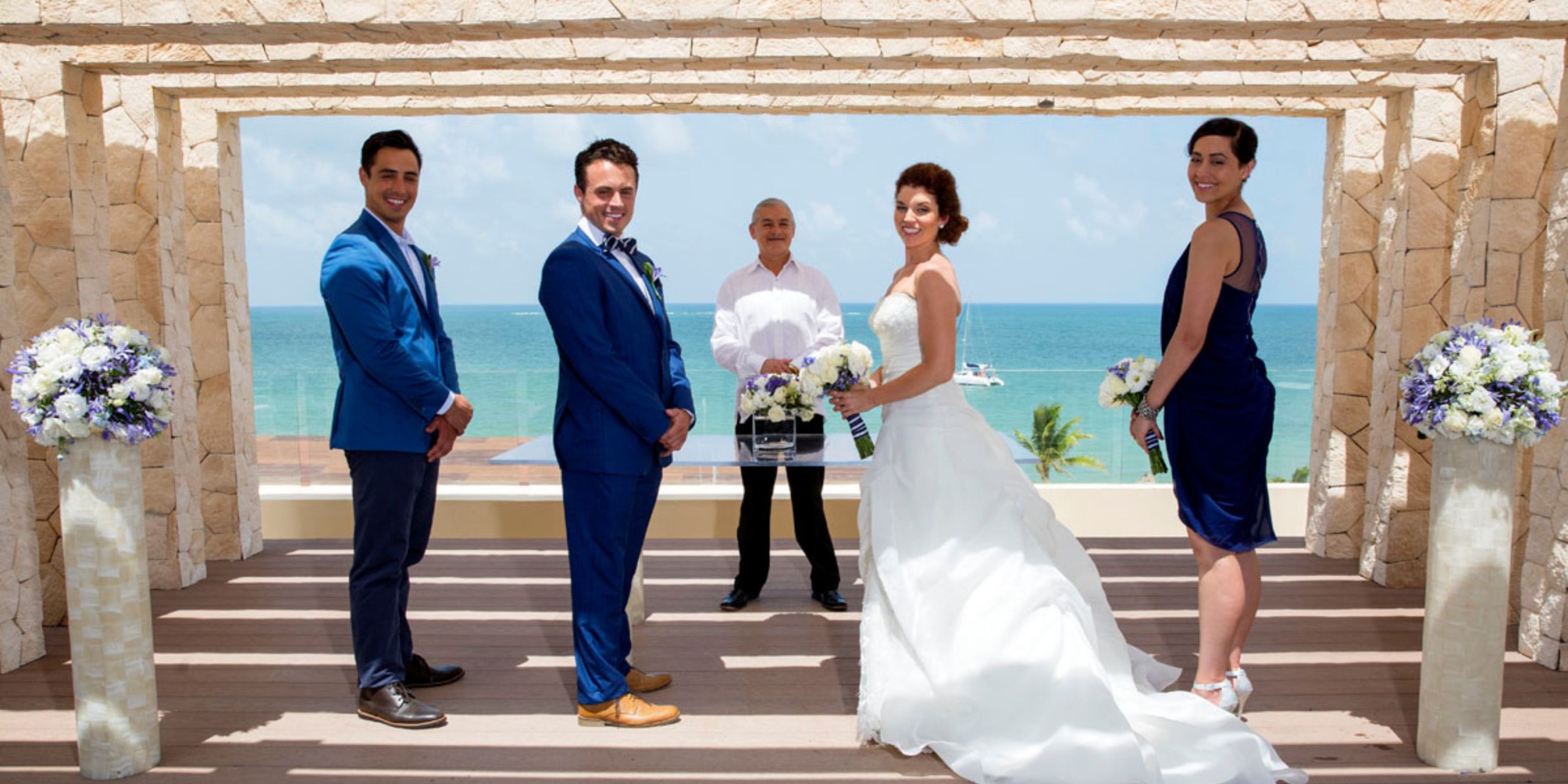 The bride and groom, along with their attendants, stand at the beachfront altar of Hideaway Royalton Cancun for a beautiful destination wedding.