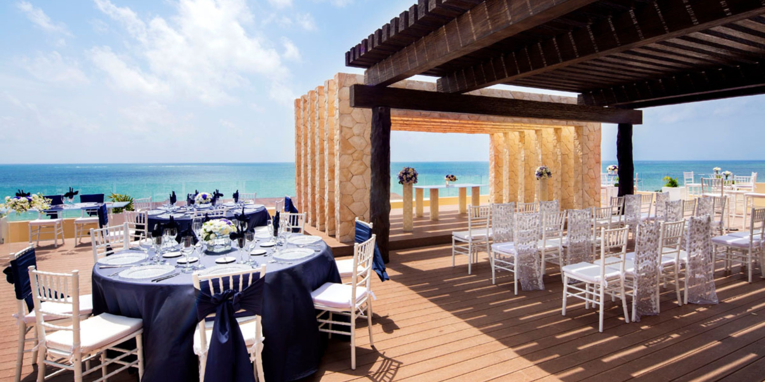 Experience a destination wedding at Hideaway Royalton Riviera Cancun, featuring elegantly decorated tables and white chairs set against the stunning backdrop of an ocean view.