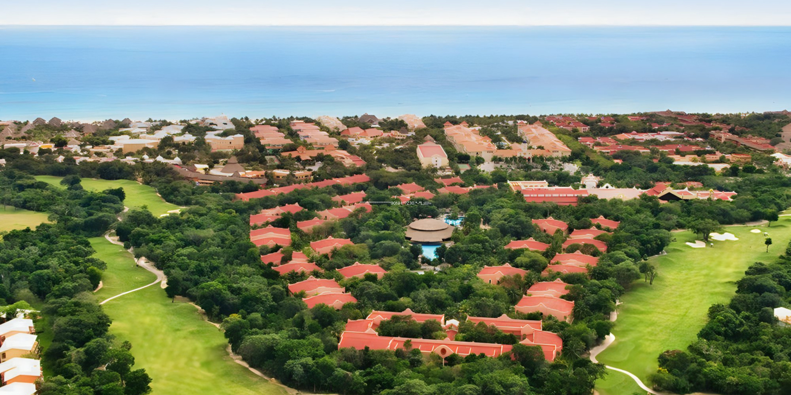 Aerial view of Hotel Riu Tequila, a luxury resort destination wedding with red-tiled roofs surrounded by lush greenery near a coastline.