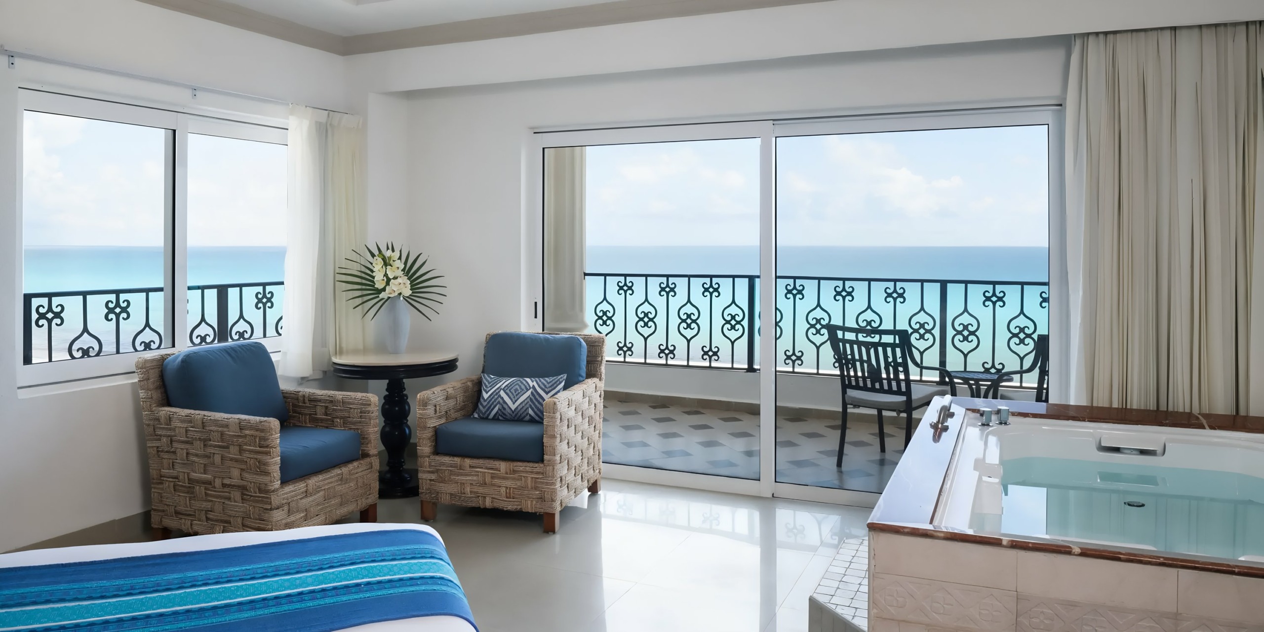 Hyatt Zilara Cancun with ocean view, featuring a king-size bed, wicker chairs, a hot tub, balcony, and large sliding glass doors.