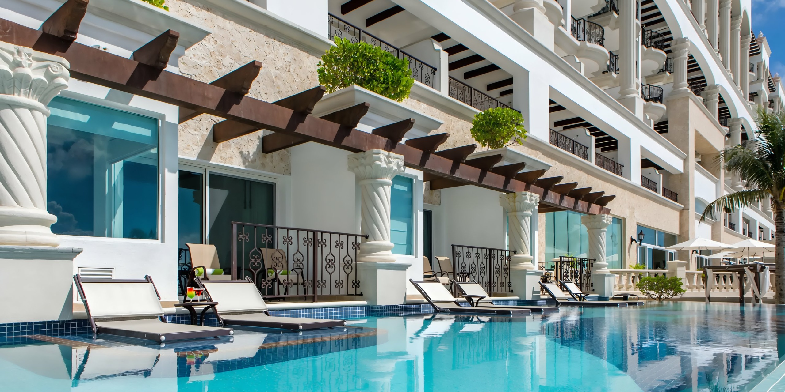 Hyatt Zilara Cancun poolside area with loungers, clear blue water, and a white multi-story building with balconies and columns.