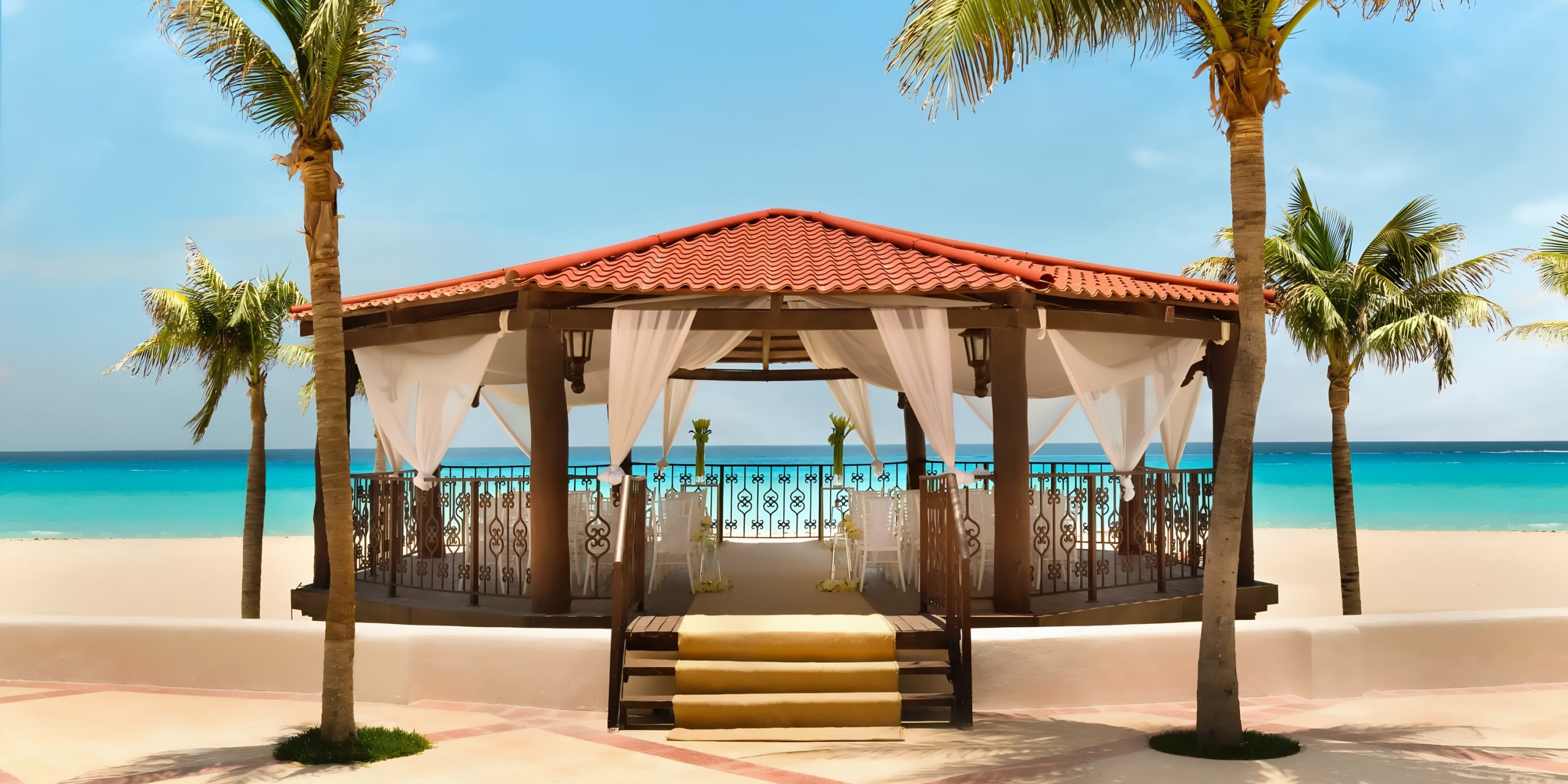 A Hyatt Zilara Cancun with white curtains, red tile roof, flanked by palm trees, overlooking a turquoise sea.