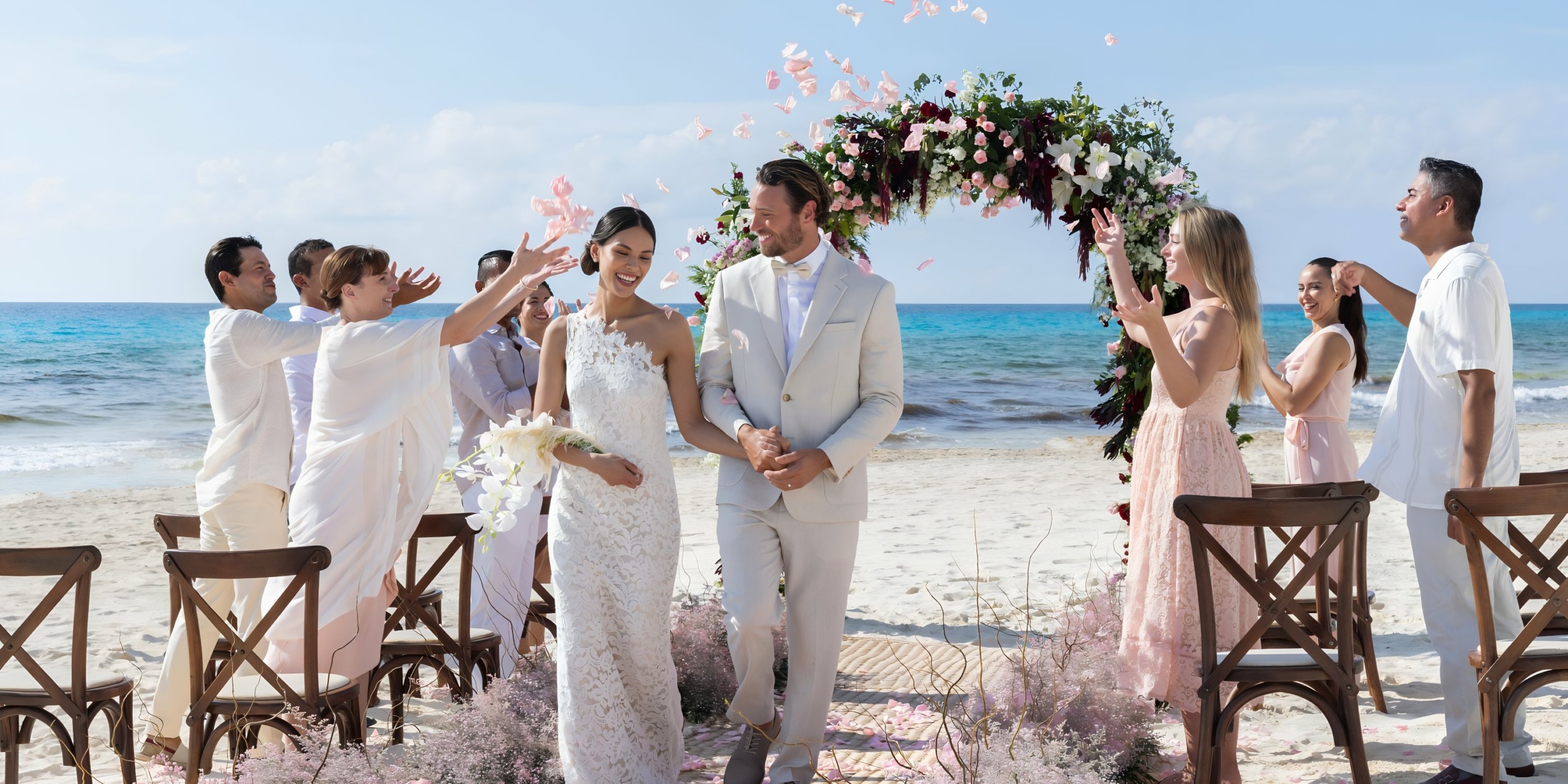 A wedding ceremony on the beach at Hyatt Zilara Cancun with guests throwing flower petals at the smiling bride and groom under a floral arch.