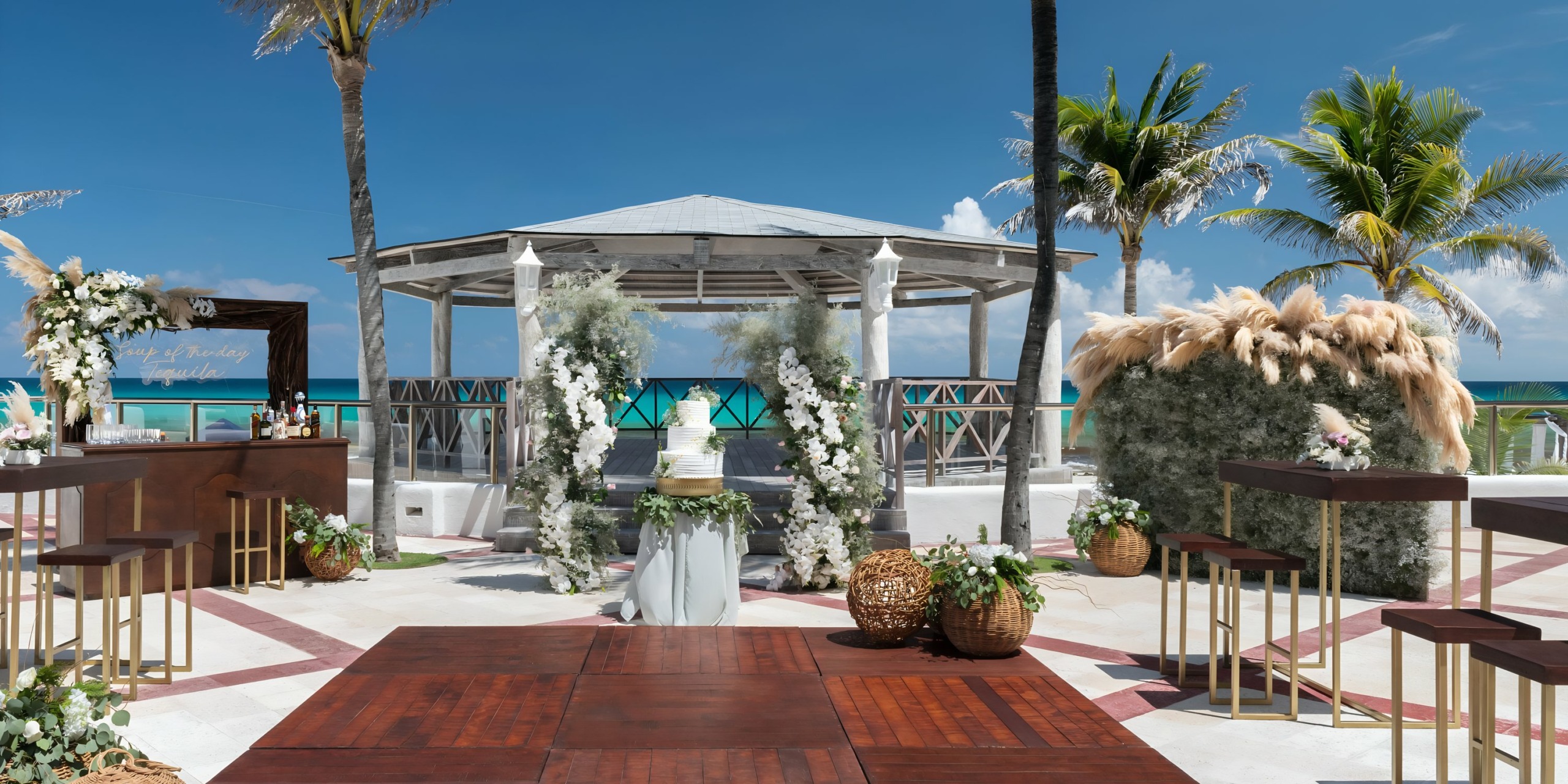 Hyatt Zilara Cancun beachfront wedding setup with floral decorations, an aisle leading to a gazebo, and palm trees under a clear blue sky.
