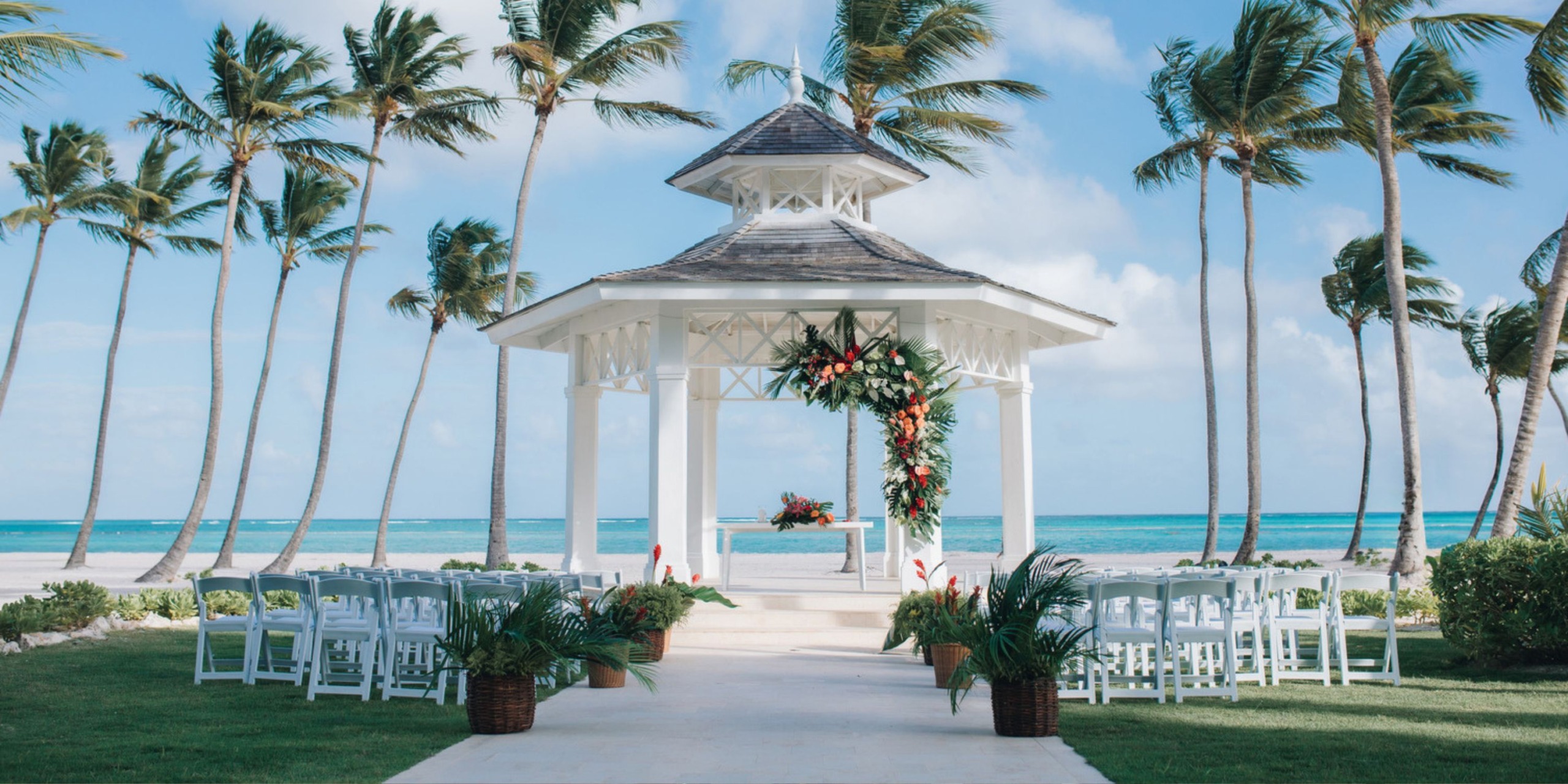 Hyatt Zilara Cap Cana provides the perfect setting for a destination wedding on the beach, complete with elegant chairs, beautiful flowers, and swaying palm trees.