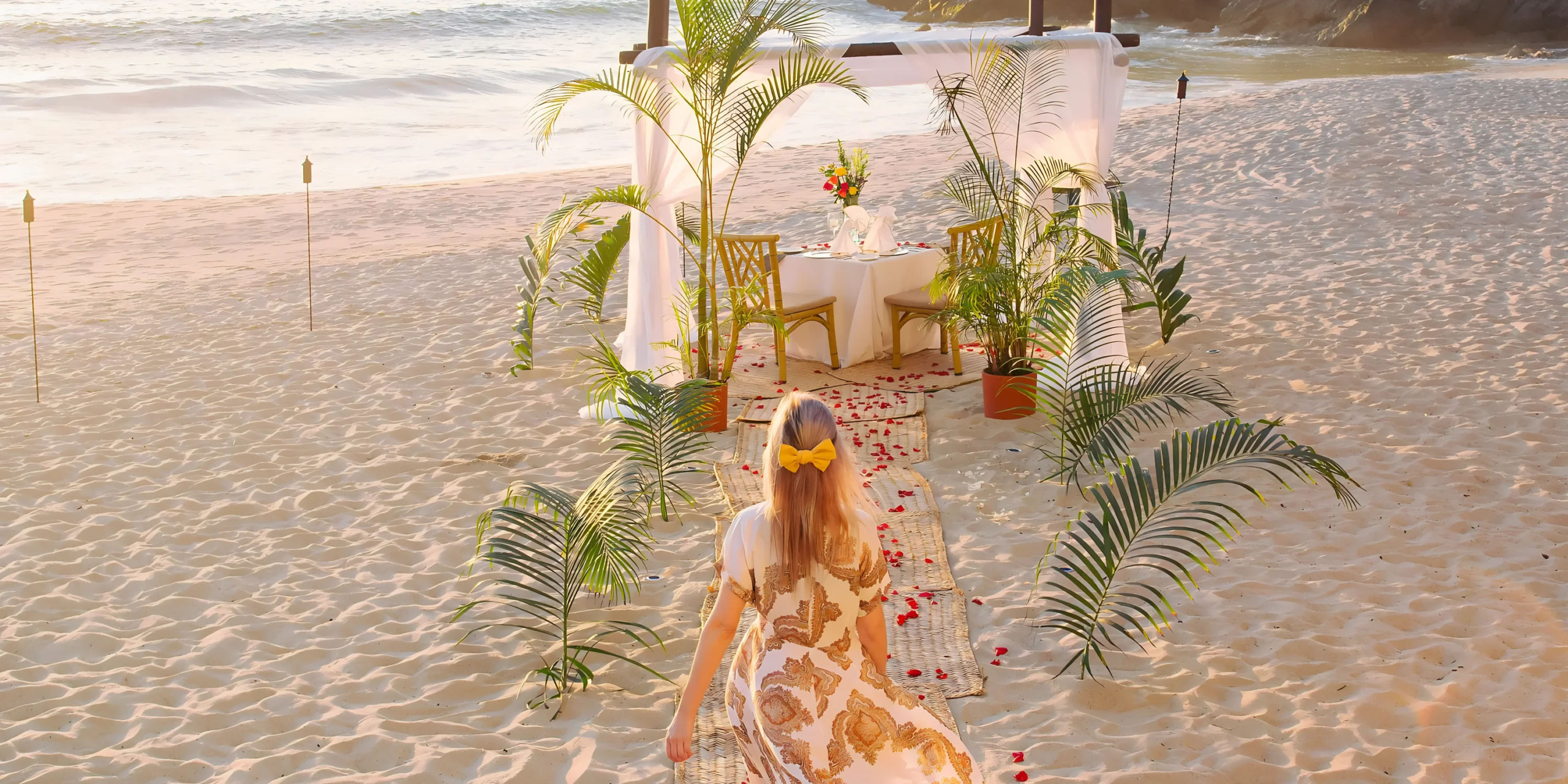 Woman approaching a romantic beach dining setup at sunset at Hyatt Ziva Puerto Vallarta.