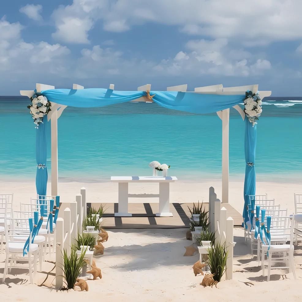 Outdoor beach wedding setup featuring a white pergola adorned with blue fabric and flowers, white chairs with blue ribbons, and a small altar table, all set against the backdrop of the ocean.