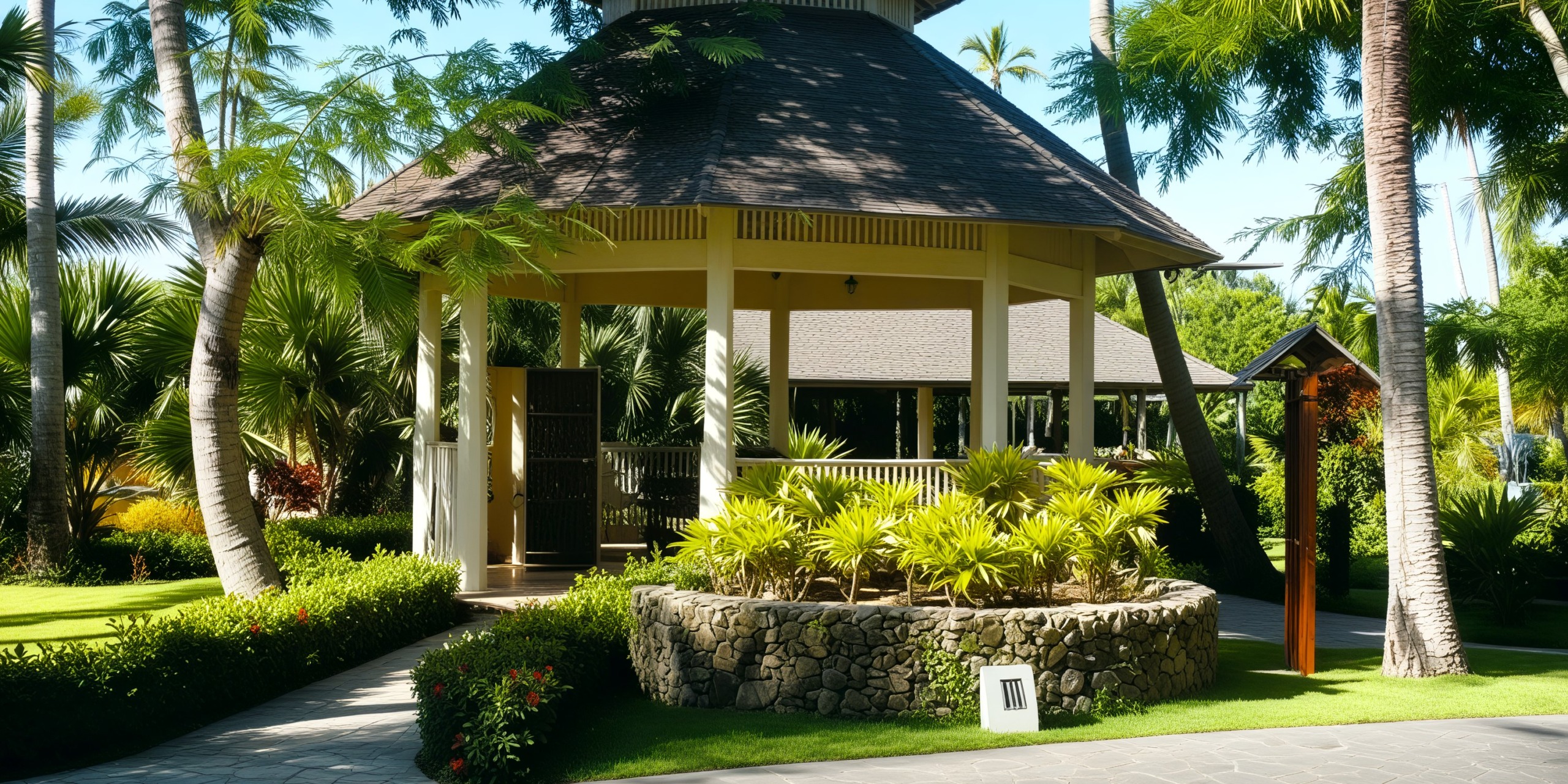 A pavilion perfect for a destination wedding is nestled amidst lush tropical trees and plants, setting a stunning scene on a sunny day.