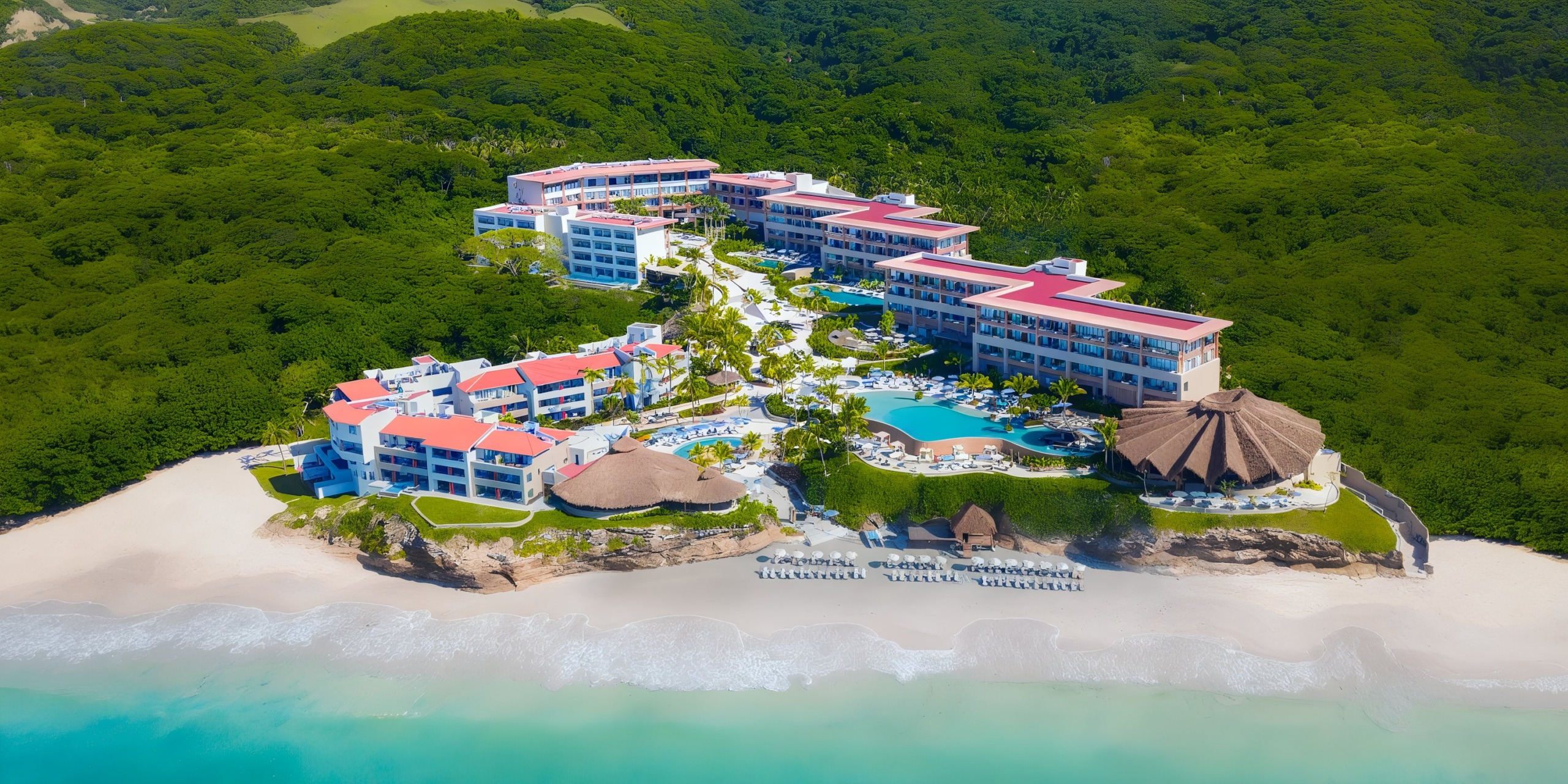 Aerial view of Marival Armony, a beachfront resort featuring red-roofed buildings, multiple pools, and lush greenery surrounding it, nestled by the ocean.