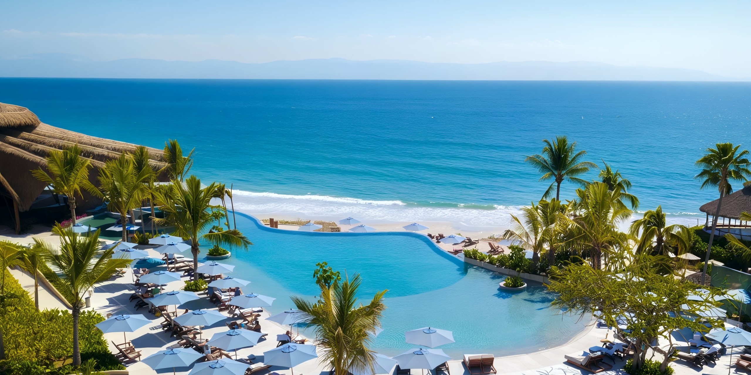 The infinity pool at Marival Armony offers a stunning view of the beach with its tranquil ocean waves, while palm trees and lounge chairs equipped with umbrellas envelop the pool area.