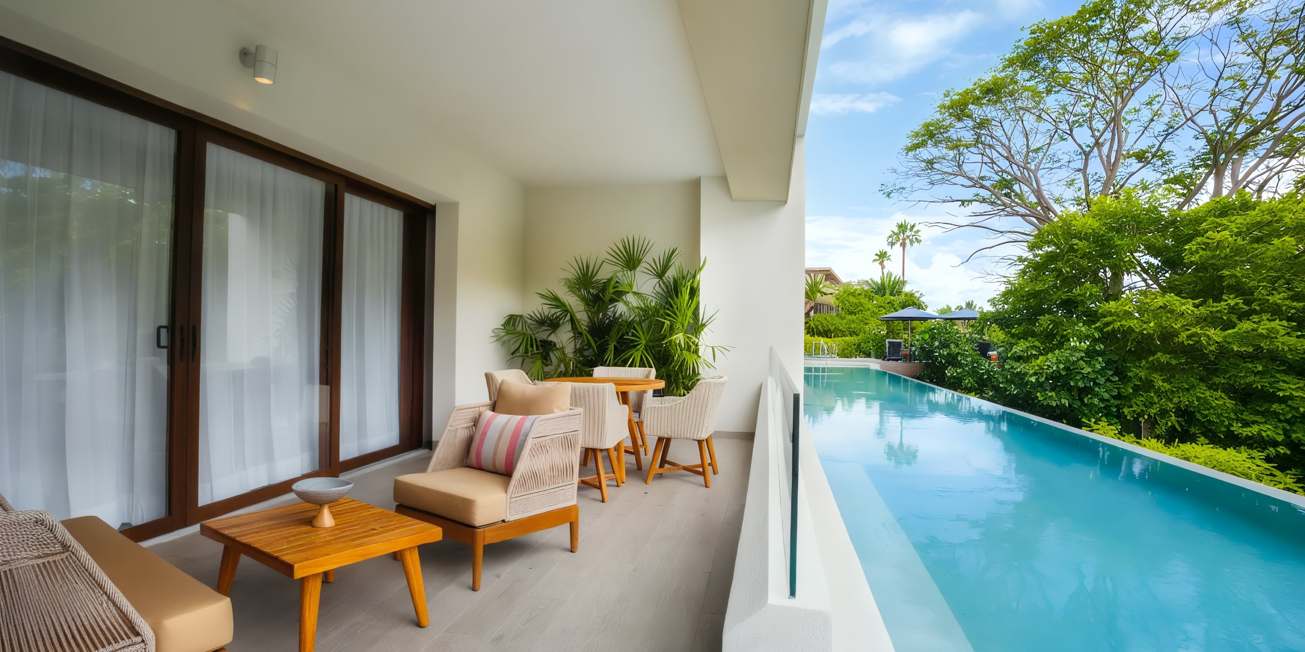 Experience the outdoor terrace at Marival Armony, featuring a seating area by a modern infinity pool, beautifully surrounded by lush greenery under a clear blue sky.