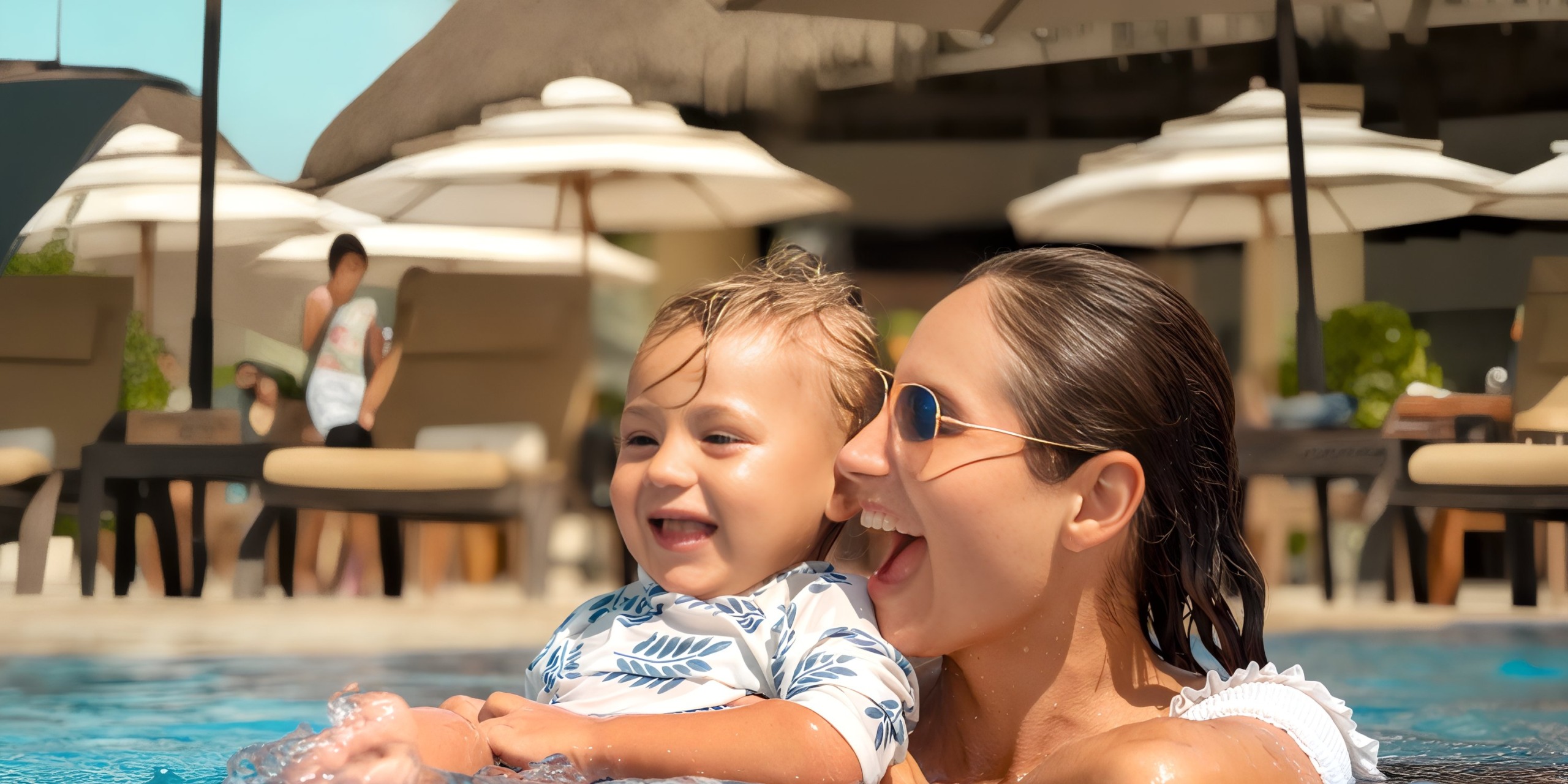 A woman and child are smiling while swimming in the pool at Marival Distinct, with umbrellas and lounge chairs in the background.