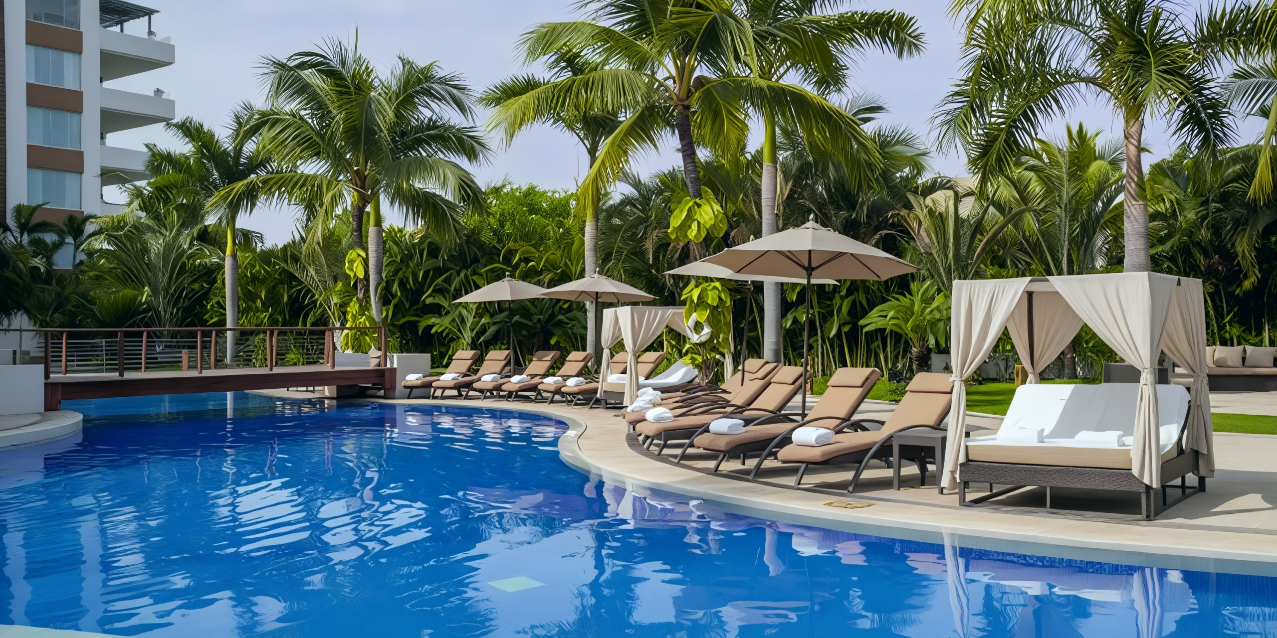 The Marival Distinct outdoor pool area is beautifully enhanced with lounge chairs, umbrellas, and cabanas, all surrounded by lush palm trees.