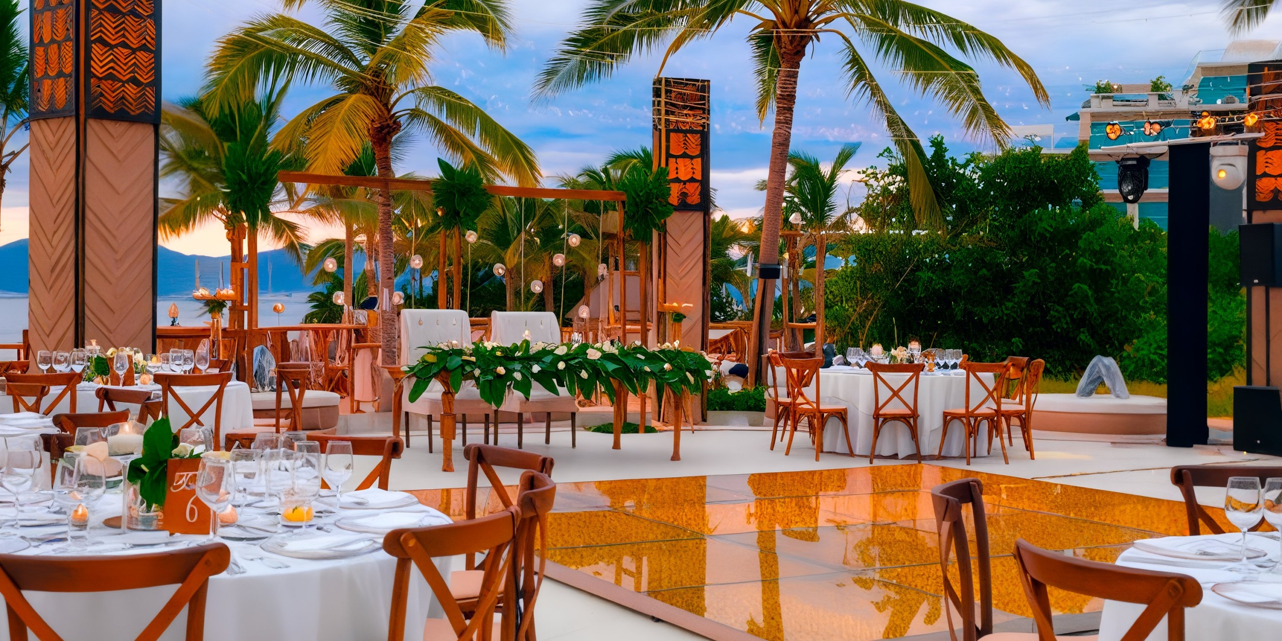 The Marival Distinct offers an outdoor wedding reception setup with elegantly arranged tables and chairs, sparkling decorative lights, lush palm trees, and a mirrored dance floor, all set against a breathtaking tropical backdrop.