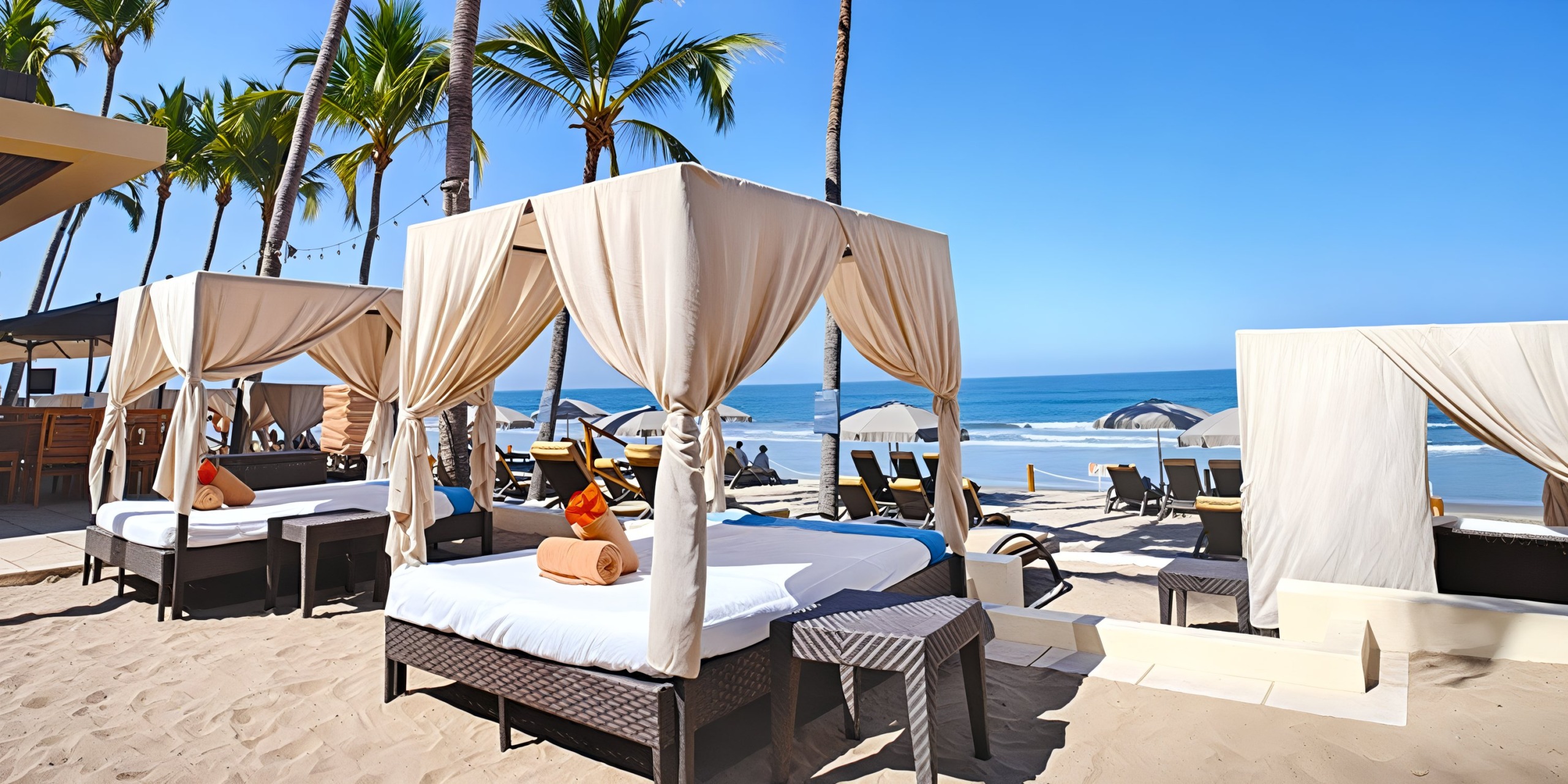 Experience the Marival Emotions: beachfront cabanas complete with canopies and lounge chairs, shaded by palm trees on a sandy beach, offering breathtaking ocean views under a clear blue sky.