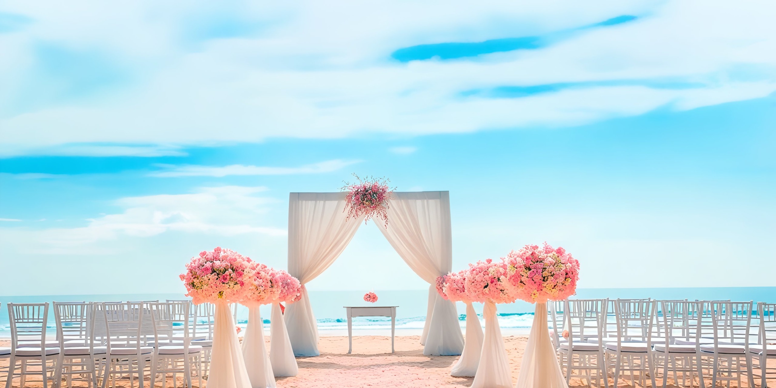 Marival Emotions offers a breathtaking beach wedding setup featuring white chairs, vibrant pink floral arrangements, and an elegantly draped archway with a stunning ocean view under a clear blue sky.