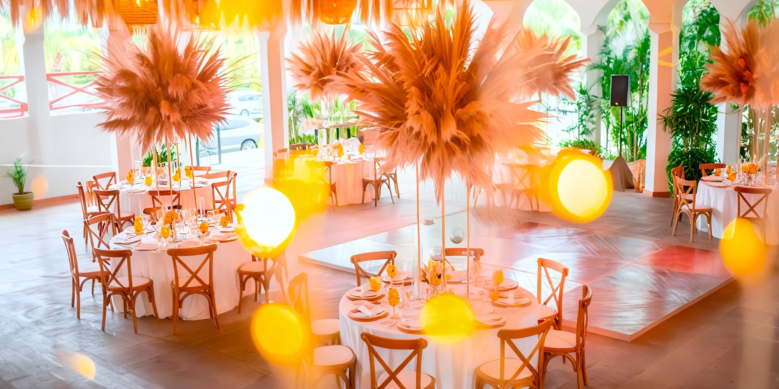 The Marival Emotions venue features round tables ready for dining, each enriched with tall floral centerpieces. Warm lighting and open archways contribute to the inviting atmosphere.