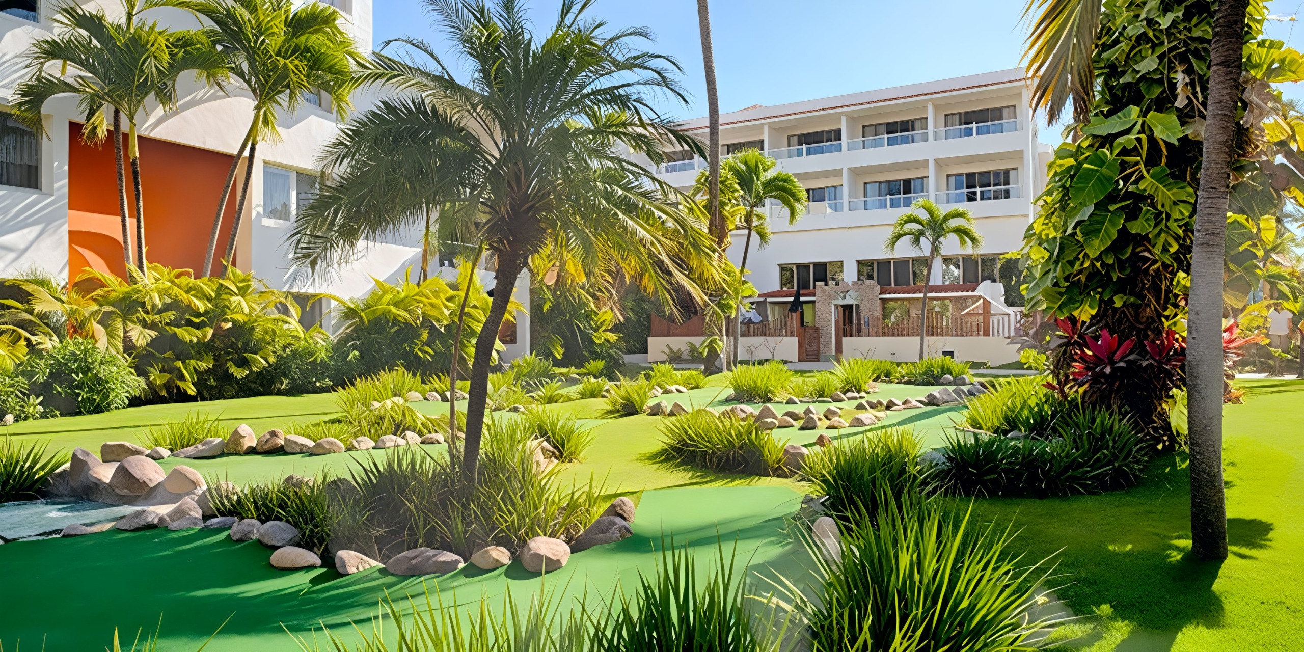 A lush garden featuring palm trees and rock-lined pathways is situated in front of the modern multi-story Marival Emotions building under a clear blue sky.