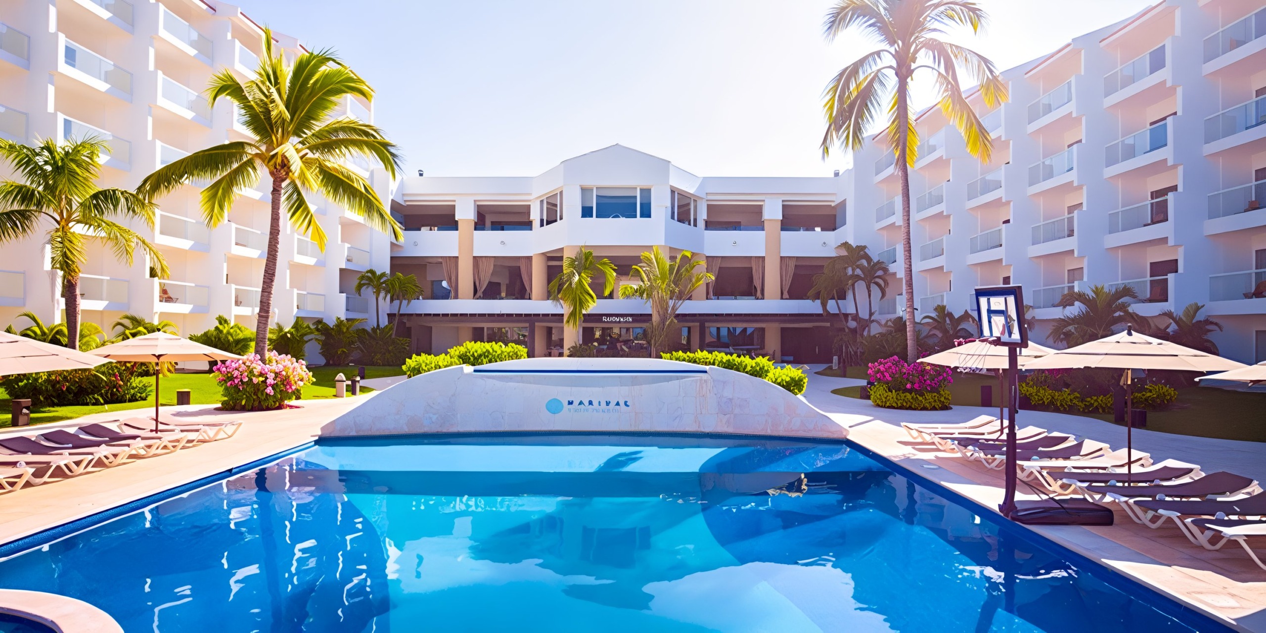 The pool at Marival Emotions is surrounded by lounge chairs, palm trees, and features a multi-story hotel building in the background.