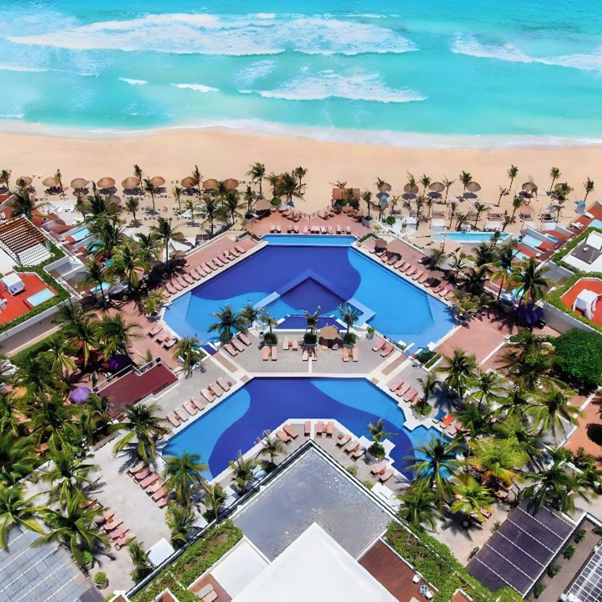 Aerial view of NOW Emerald Cancun resort with a star-shaped pool, surrounded by palm trees and loungers, located beside a turquoise sea and sandy beach, popular for destination weddings.