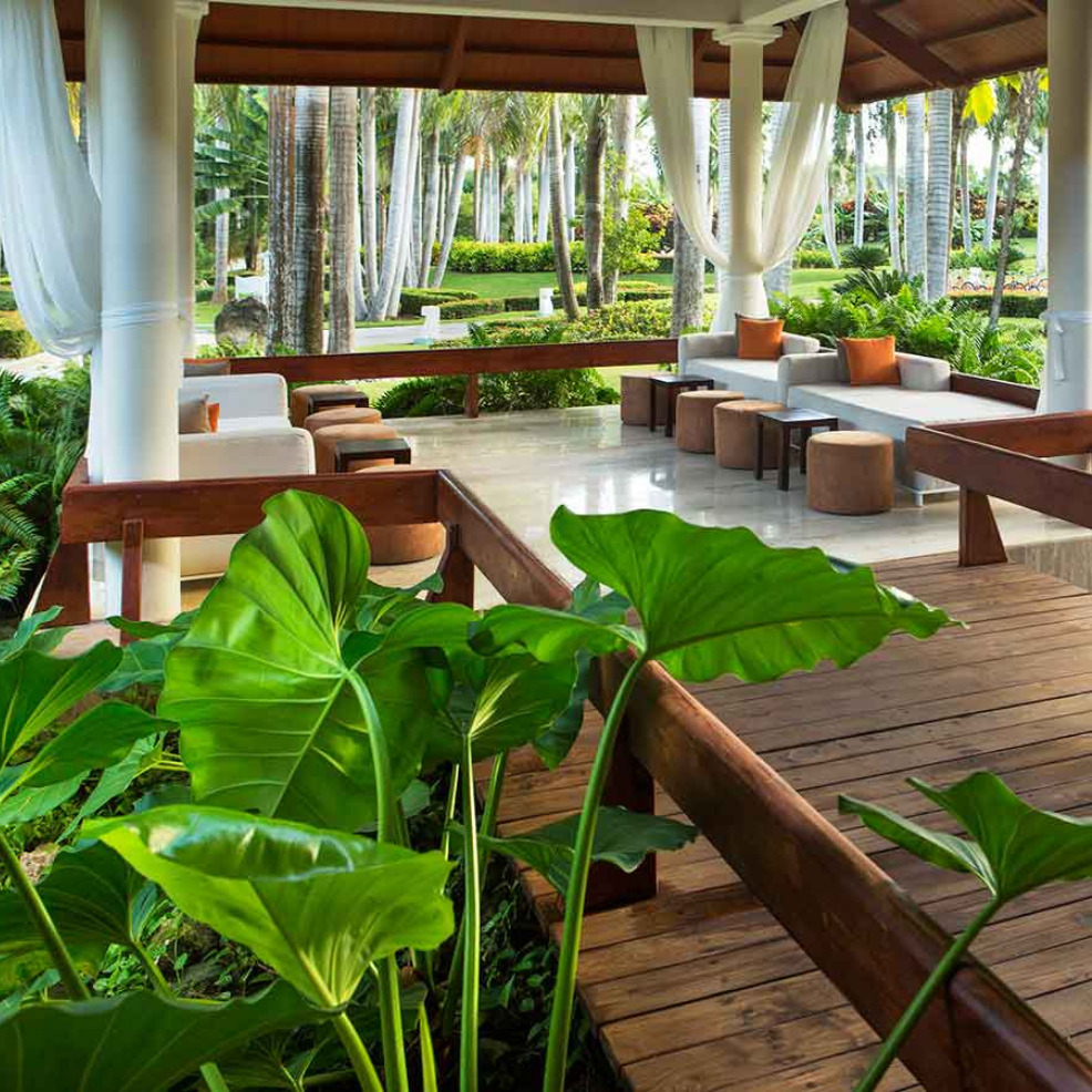 Outdoor resort pavilion perfect for destination weddings, with white columns, modern furniture, and lush greenery, featuring a polished stone floor and wooden pathway.