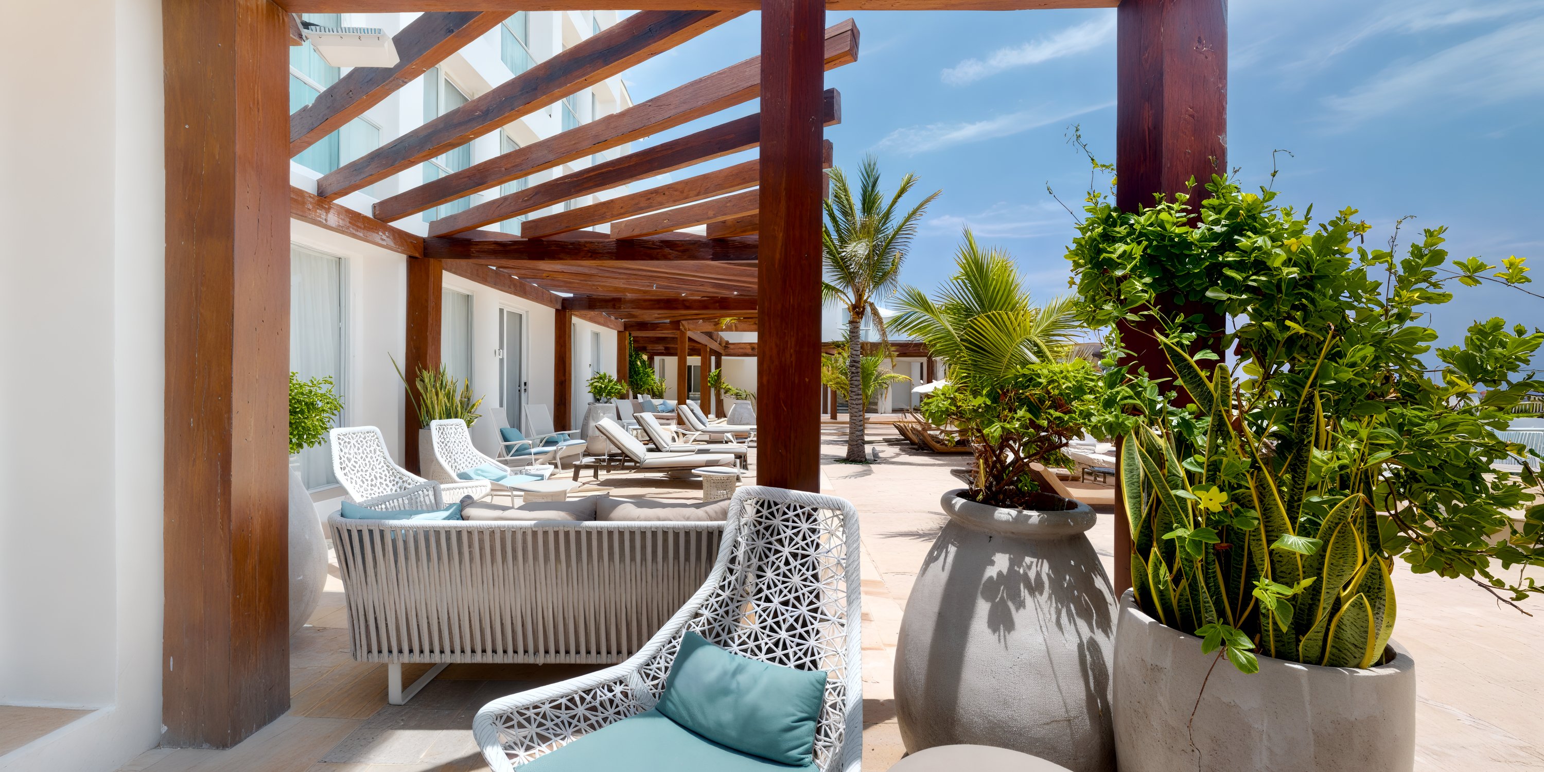 Playacar Palace: perfect for a destination wedding, features wicker chairs, loungers, and lush plants beneath a charming wooden pergola.