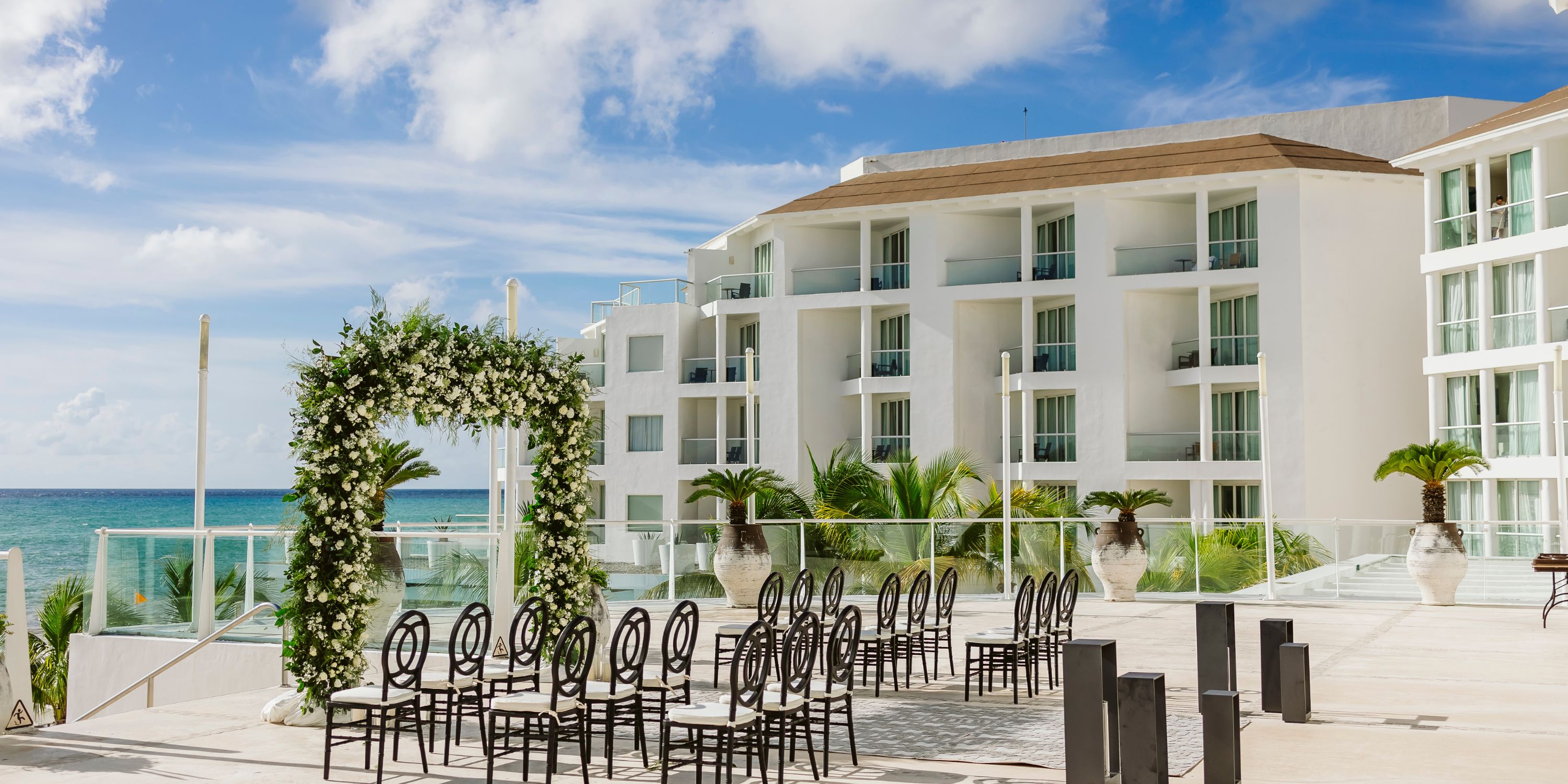 Rows of chairs face a floral arch on the patio, set for a destination wedding at Playacar Palace hotel.