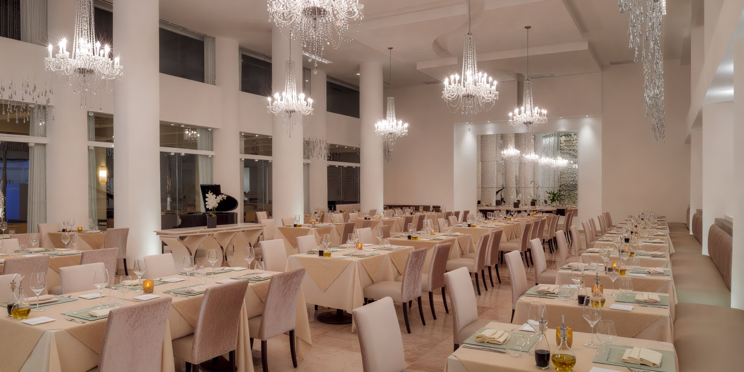Playacar Palace provides an exquisite setting for a destination wedding, featuring elegant white decor, chandeliers, and neatly arranged tables.