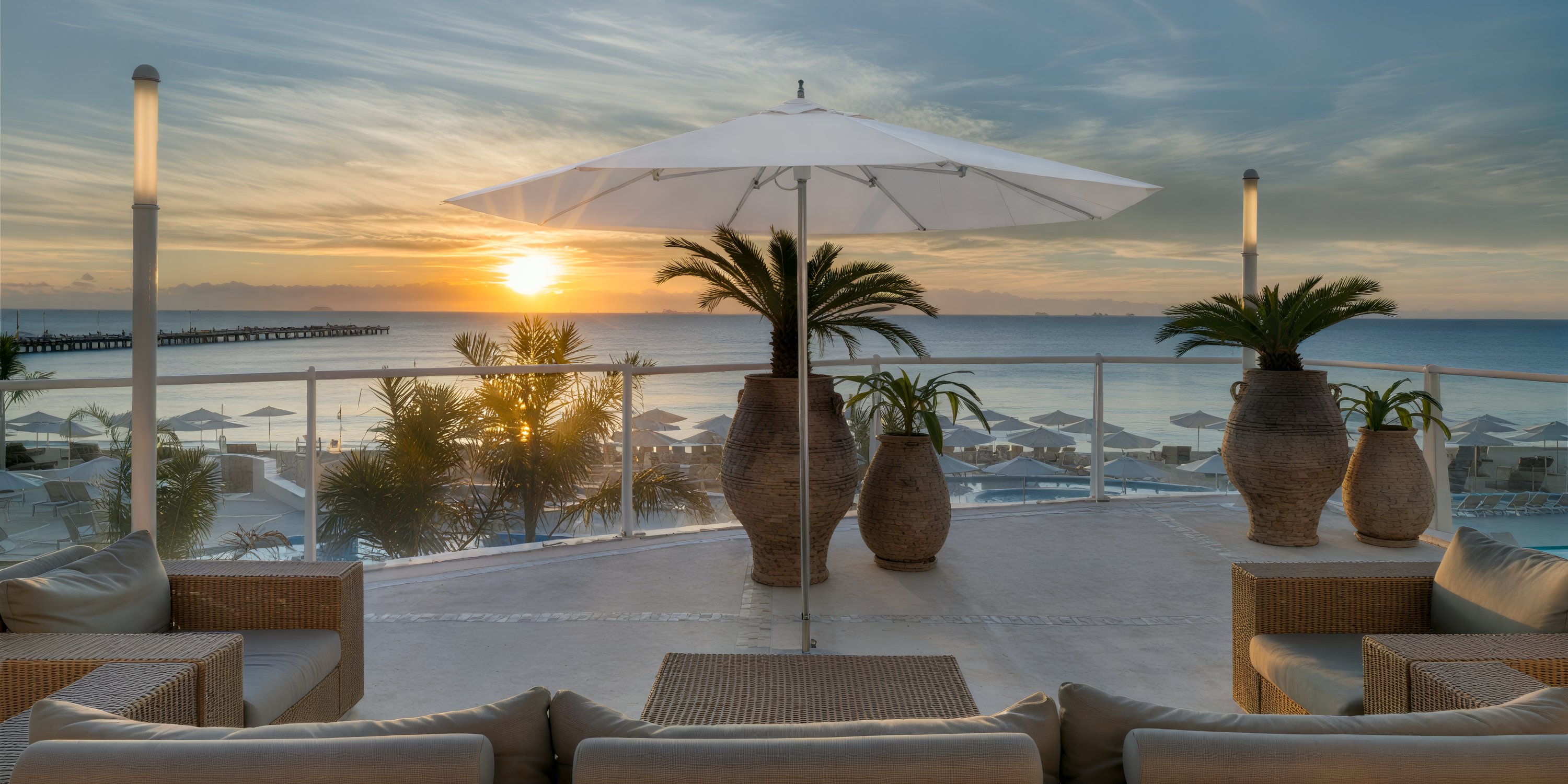 Playacar Palace: Sofas, an umbrella, and lush plants overlook the ocean at sunset, creating a breathtaking backdrop for a destination wedding.