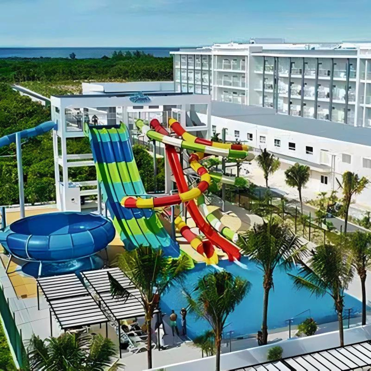 Aerial view of Hotel Riu Dunamar, a colorful water park with slides and pools next to the modern hotel, popular for destination weddings, surrounded by lush greenery.
