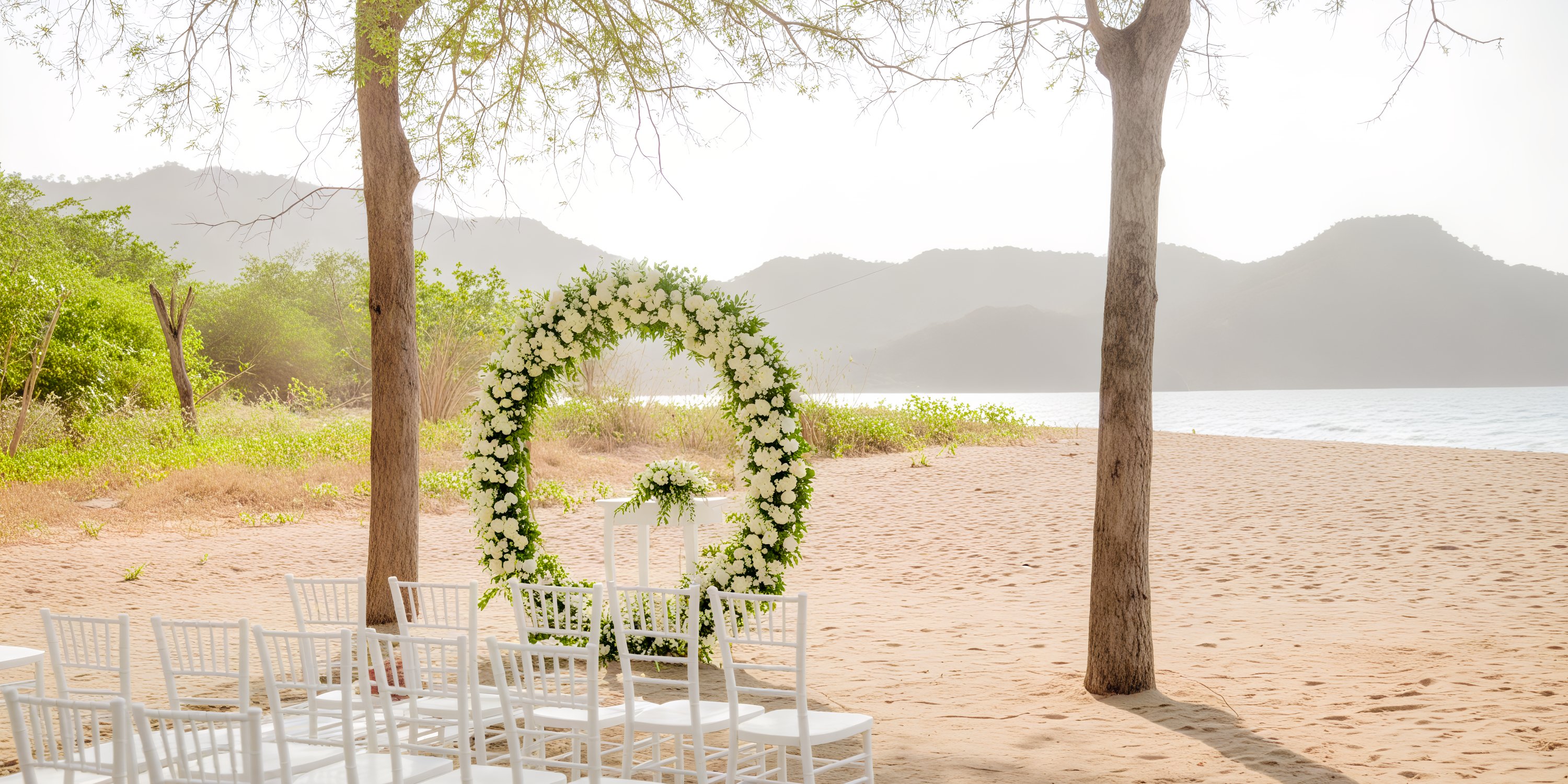 Rows of white chairs and a stunning floral arch are elegantly arranged on the beach for a destination wedding at Hotel Riu Guanacaste.