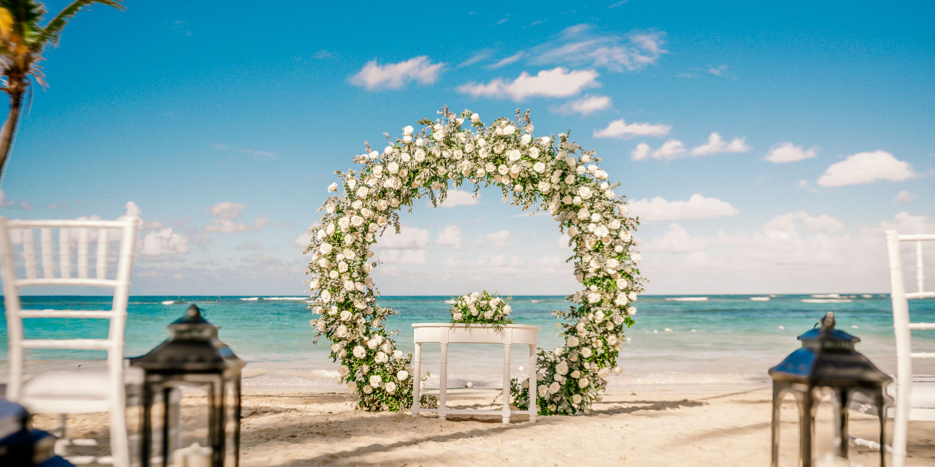 A floral wedding arch stands on sandy beach at Hotel Riu Bambu, ocean and sky creating a destination wedding backdrop.