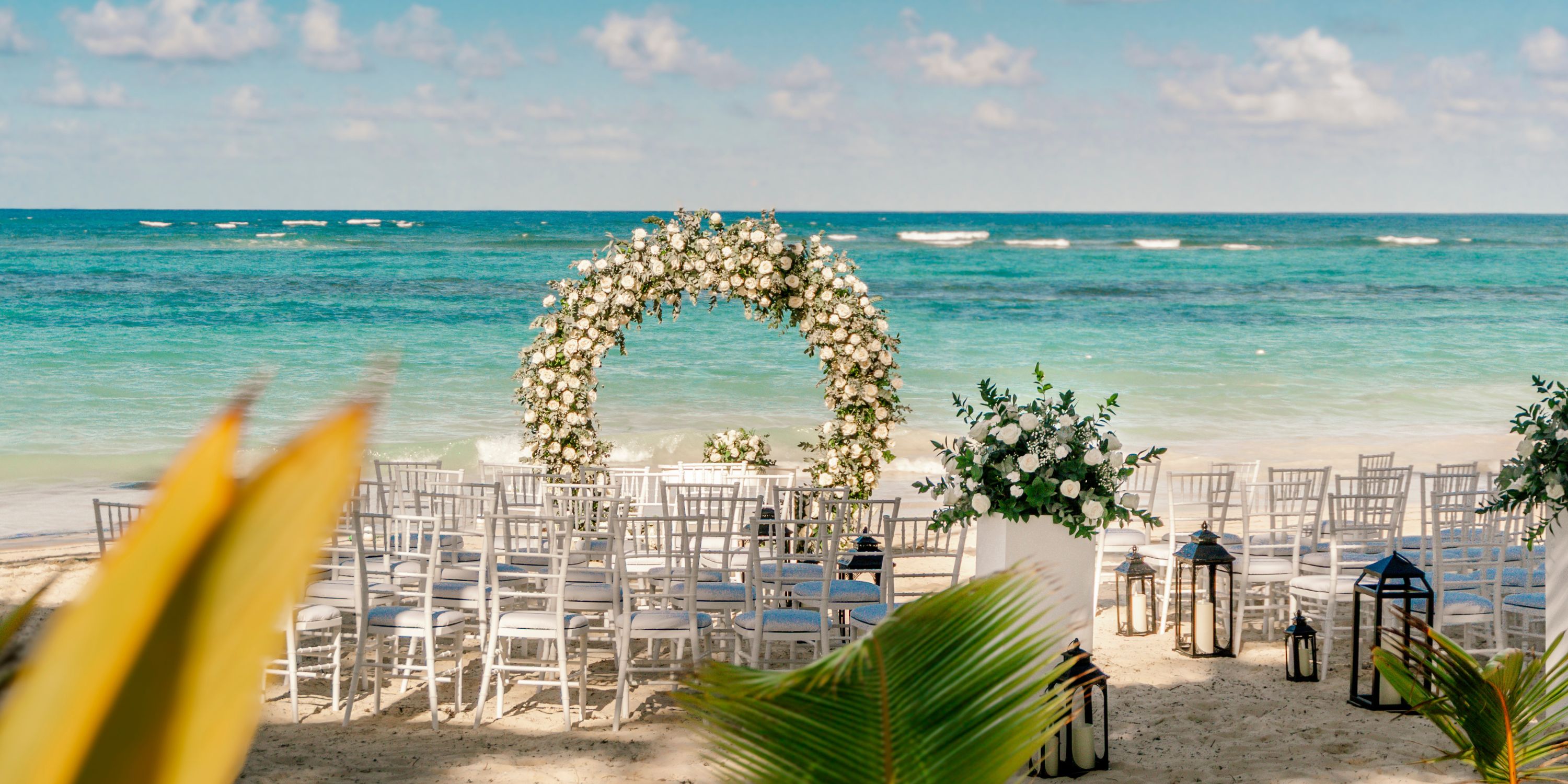 Destination wedding setup at Hotel Riu Palace Bavaro with white chairs, floral arch, and ocean backdrop.