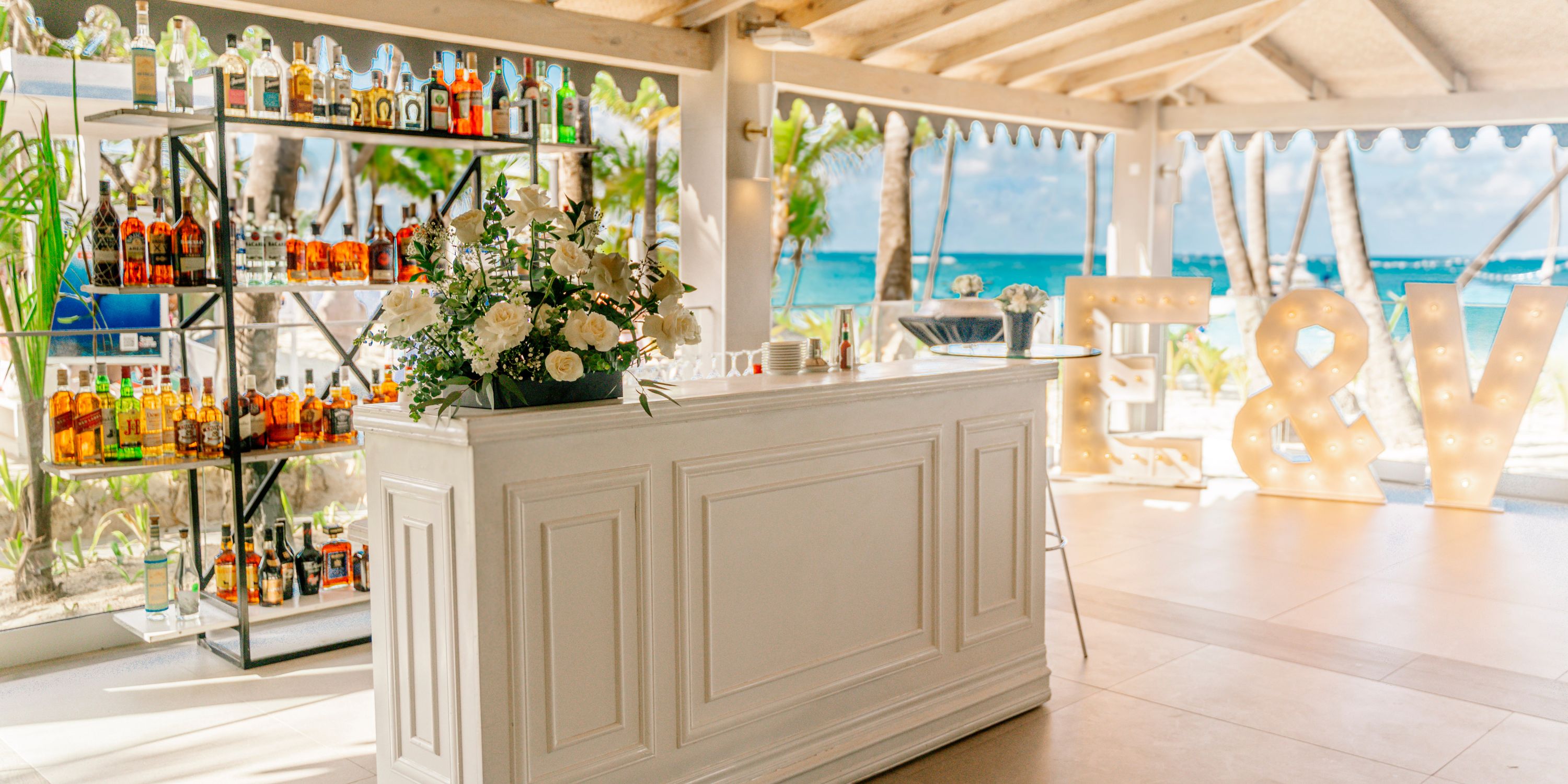 Elegant white bar with liquor bottles and flowers at Hotel Riu Palace Macao, perfect for a destination wedding.