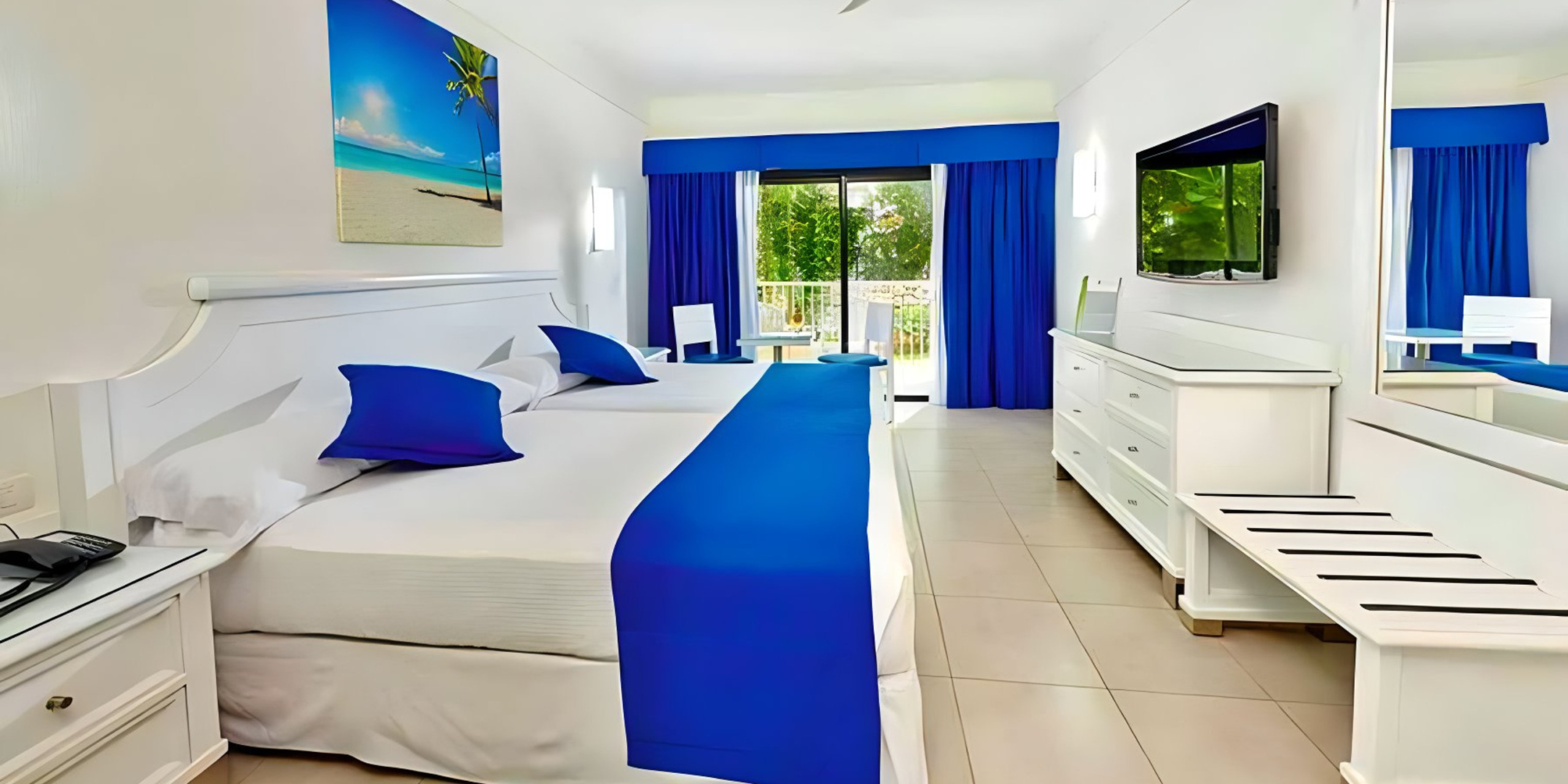 A Hotel Riu Yucatan room with blue and white bedding and a television, perfect for a destination wedding.