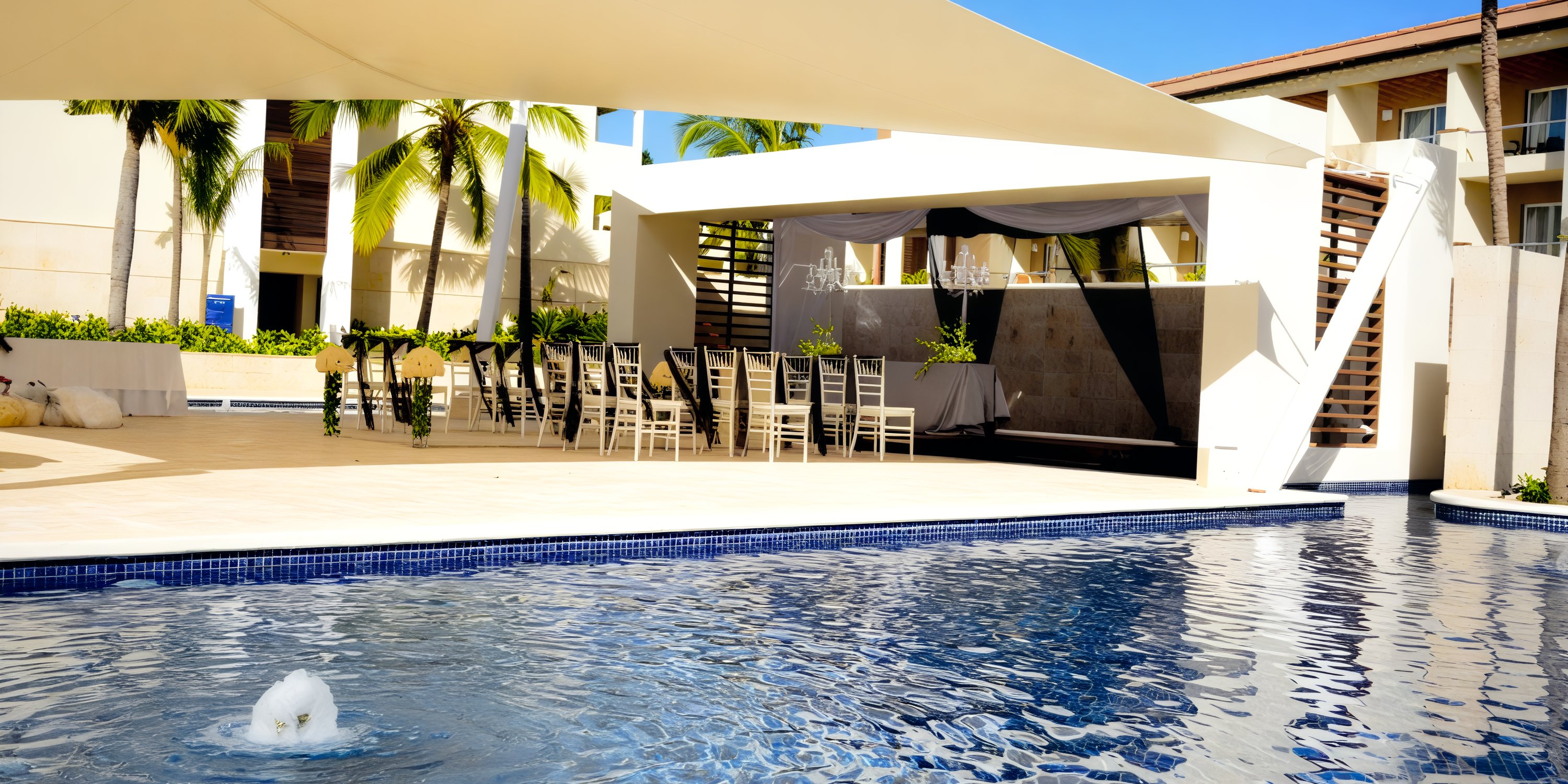 Royalton Punta Cana offers a stunning poolside area adorned with covered seating and surrounded by palm trees, making it an ideal destination for a picturesque wedding.