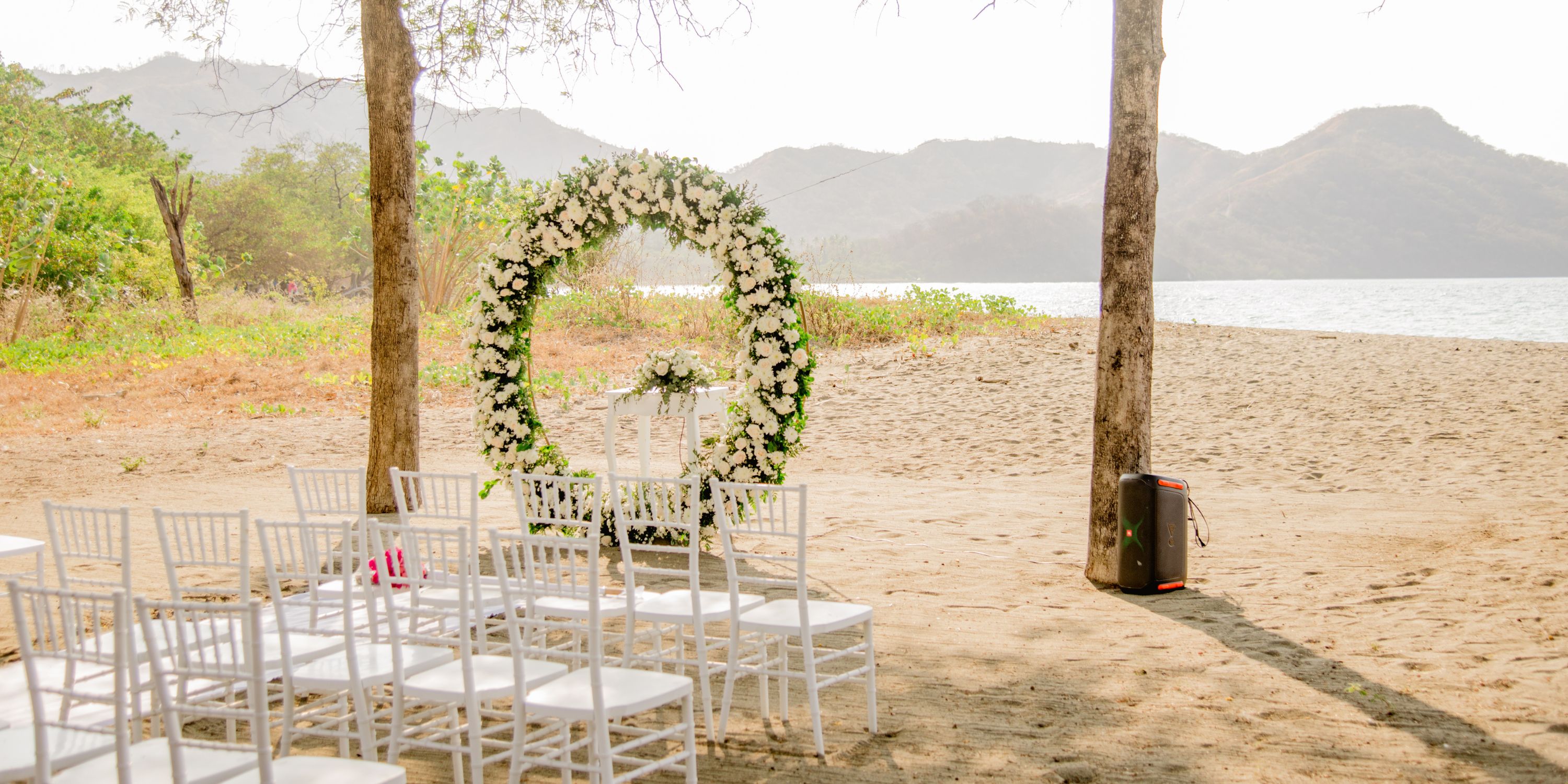 White chairs and a floral arch arranged for a destination wedding on the beach at Hotel Riu Guanacaste.