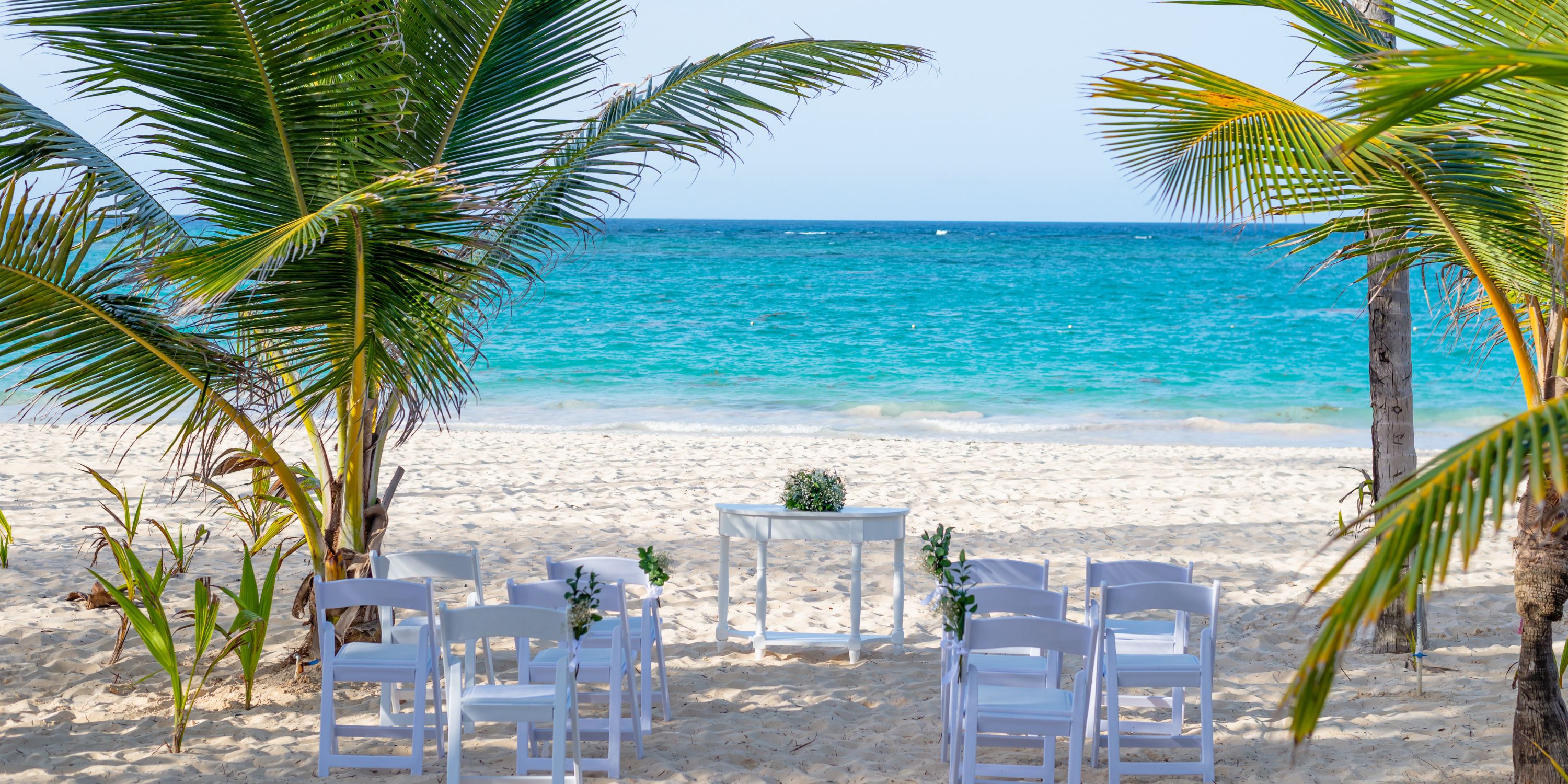 White chairs and a table arranged on the beach at Hotel Riu Palace Macao for a destination wedding.