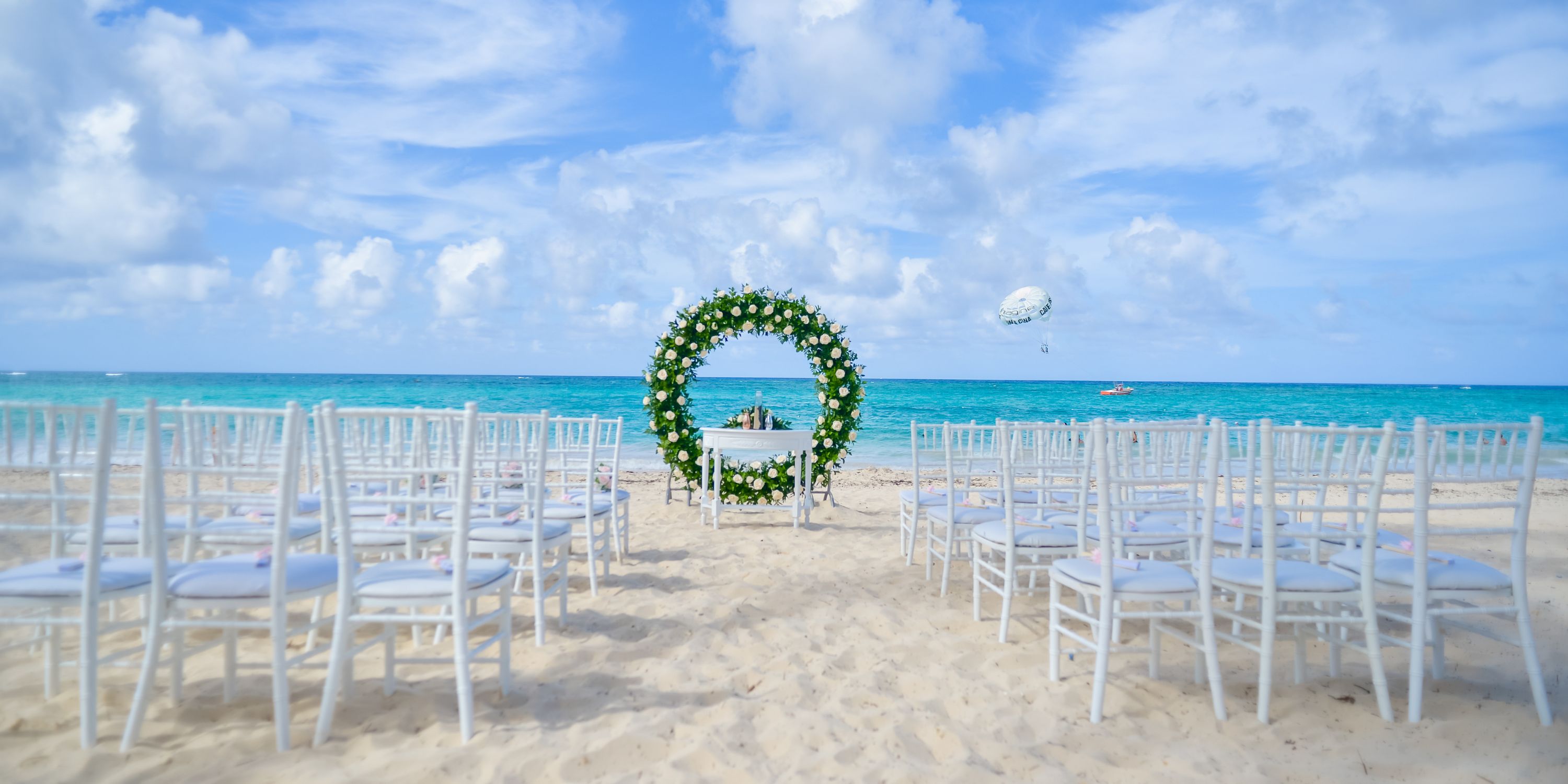 White chairs and a floral wedding arch on the beach at Hotel Riu Palace Macao, perfect for a destination wedding.