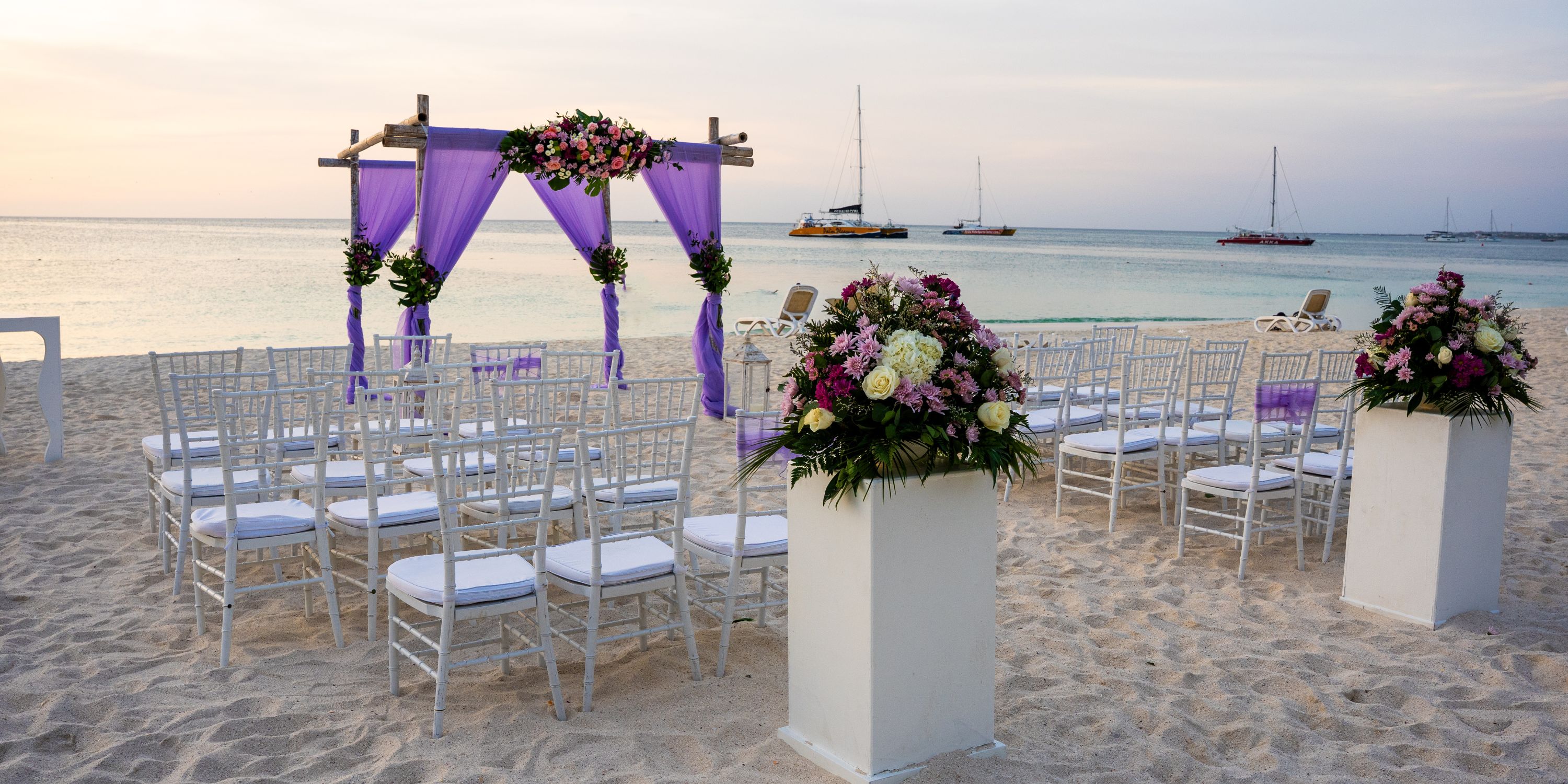 Destination wedding on the beach at Hotel Riu Palace Aruba with white chairs, florals, and a purple arch.