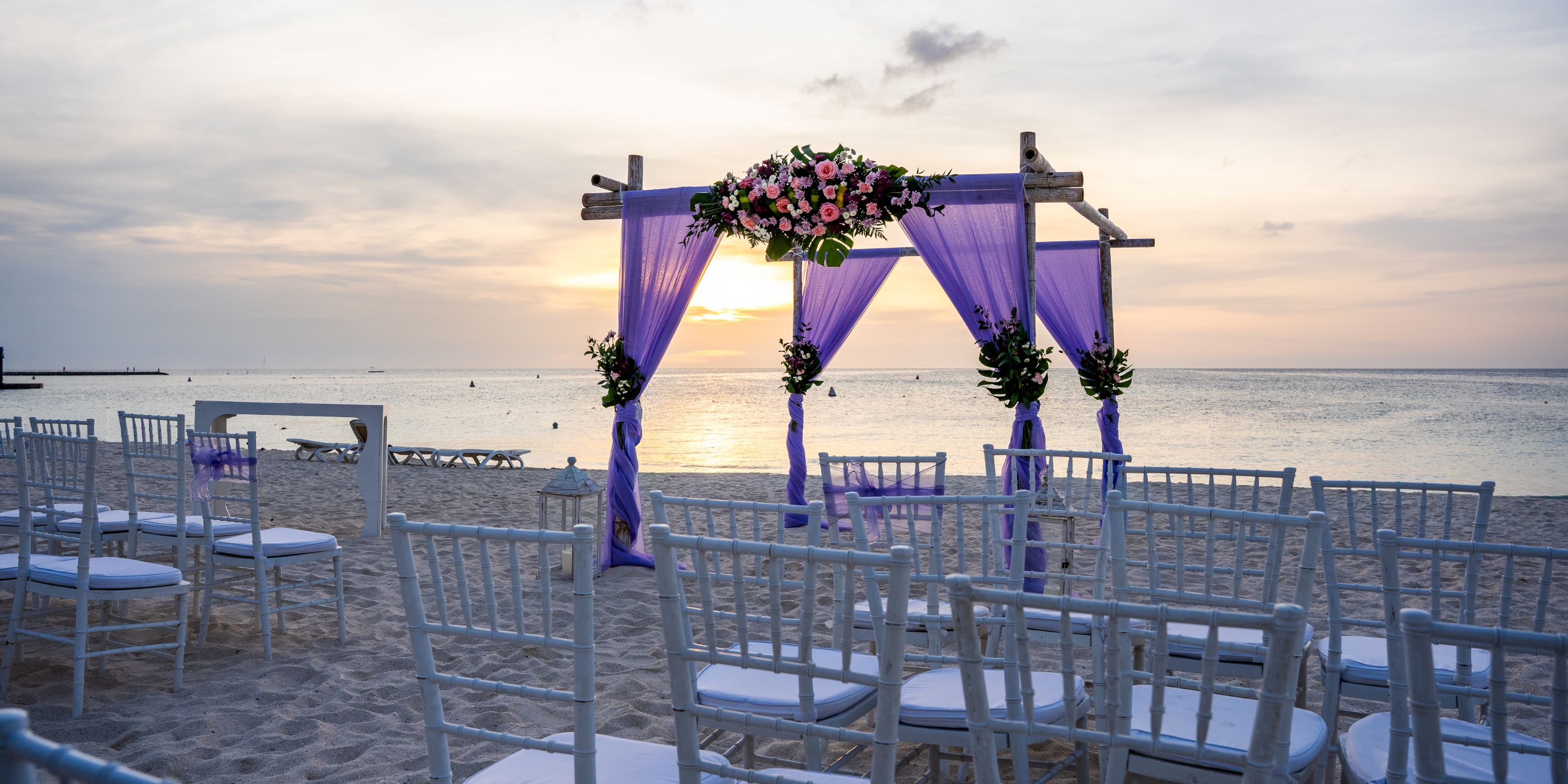 White chairs and a floral arch are arranged on the sand at Hotel Riu Palace Aruba for a destination wedding.
