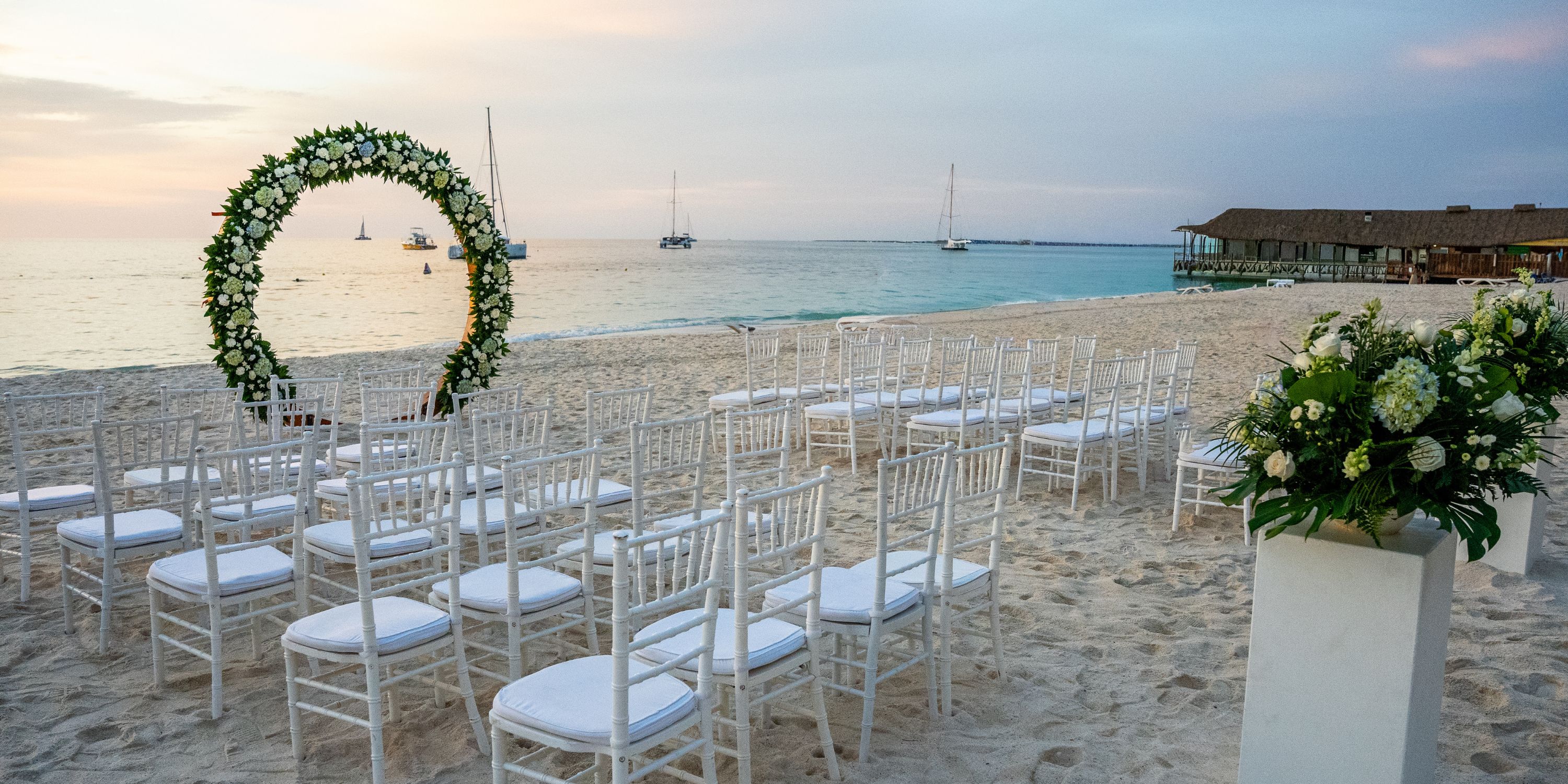White chairs and a floral arch arranged for a destination wedding at Hotel Riu Palace Aruba.