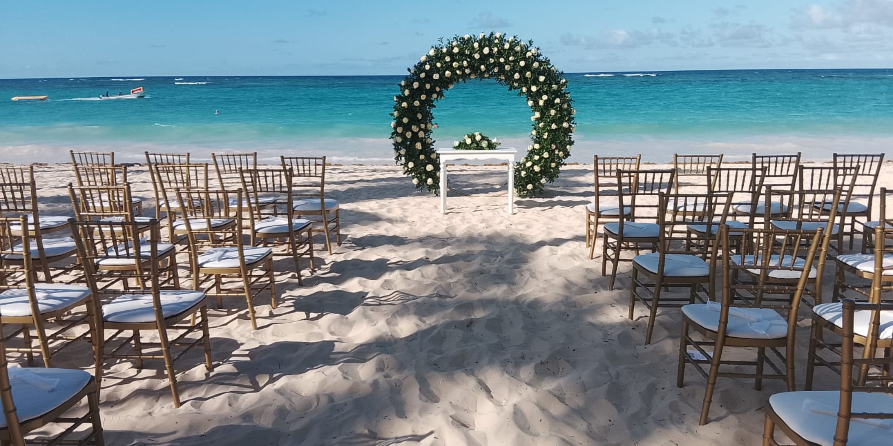 Rows of chairs face a floral arch at a beachside destination wedding at Hotel Riu Palace Bavaro.